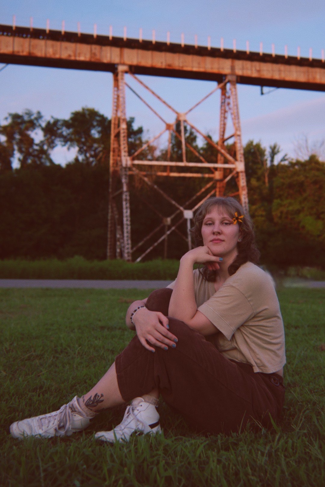 a woman sitting on the grass in front of a bridge