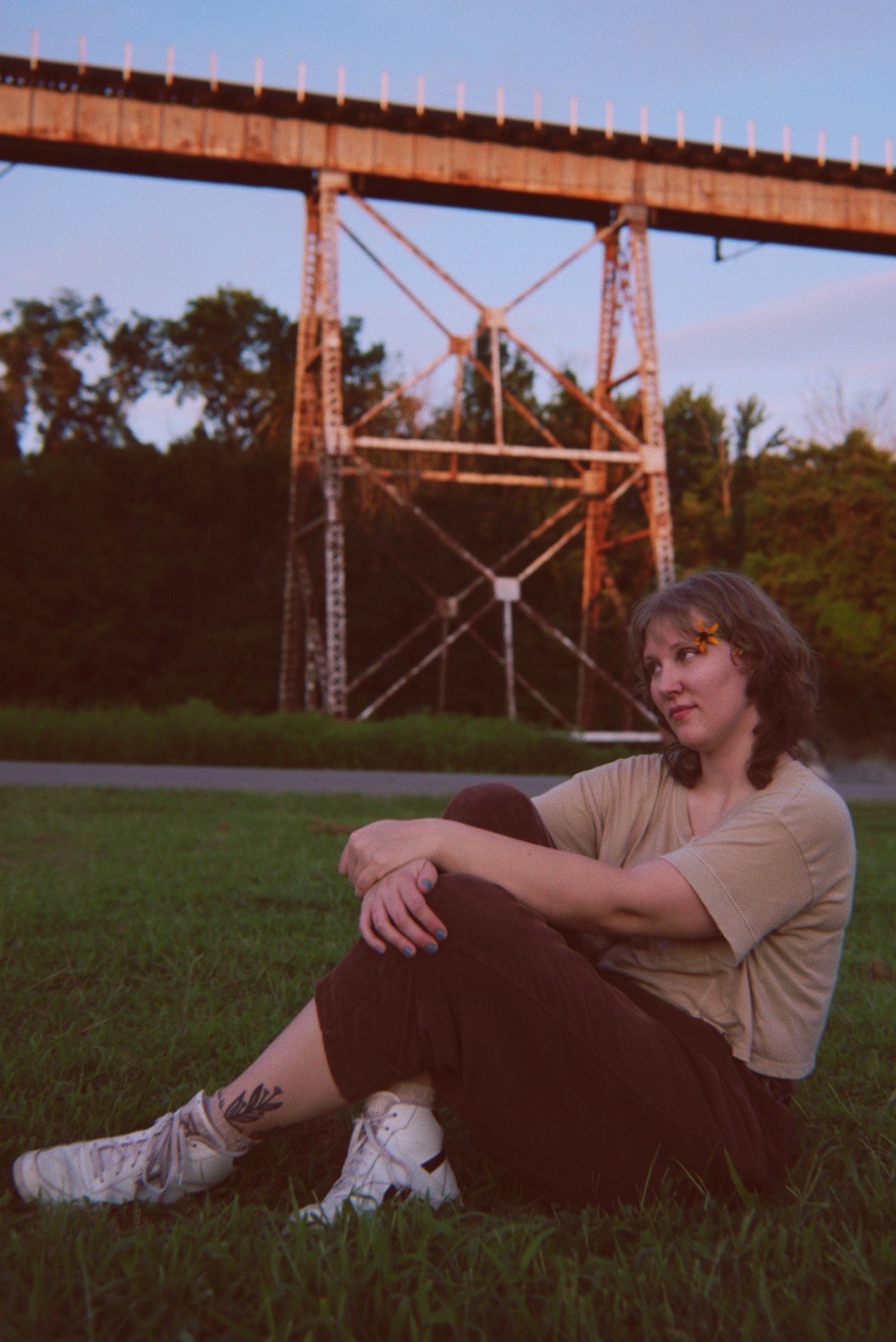 Lily Harden tip jar: a woman sitting on the grass in front of a bridge
