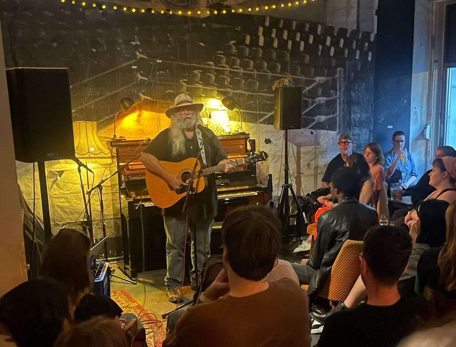 a man in a hat is playing an acoustic guitar in front of a crowd