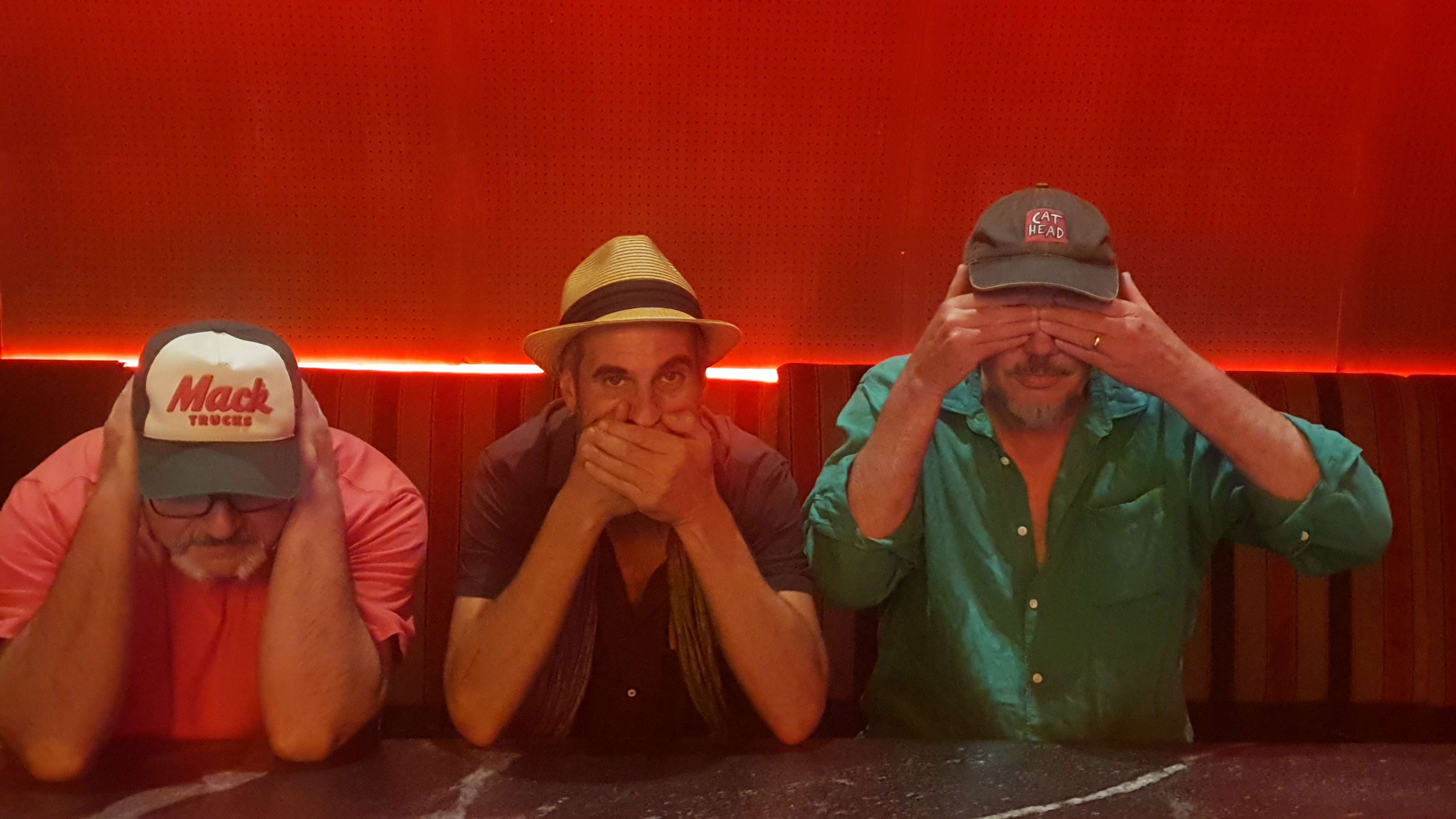 three men with hats covering their faces in front of a red background