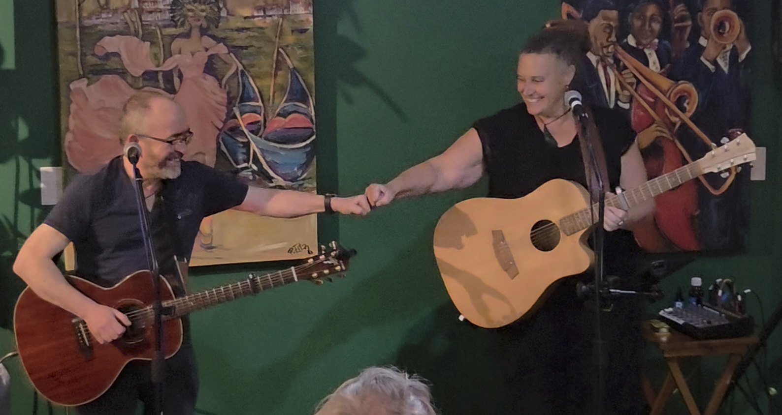 two people playing acoustic guitar in front of a painting