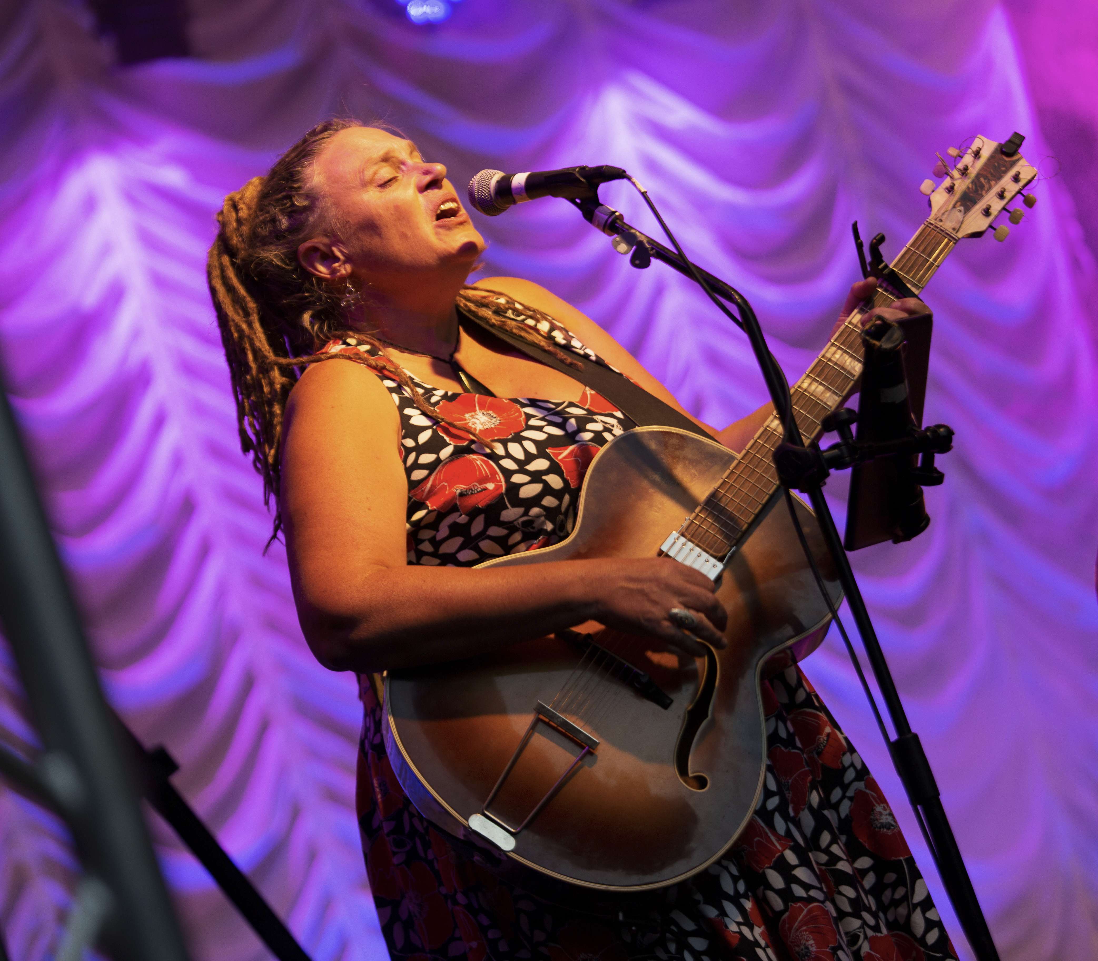 a woman singing into a microphone while playing an acoustic guitar