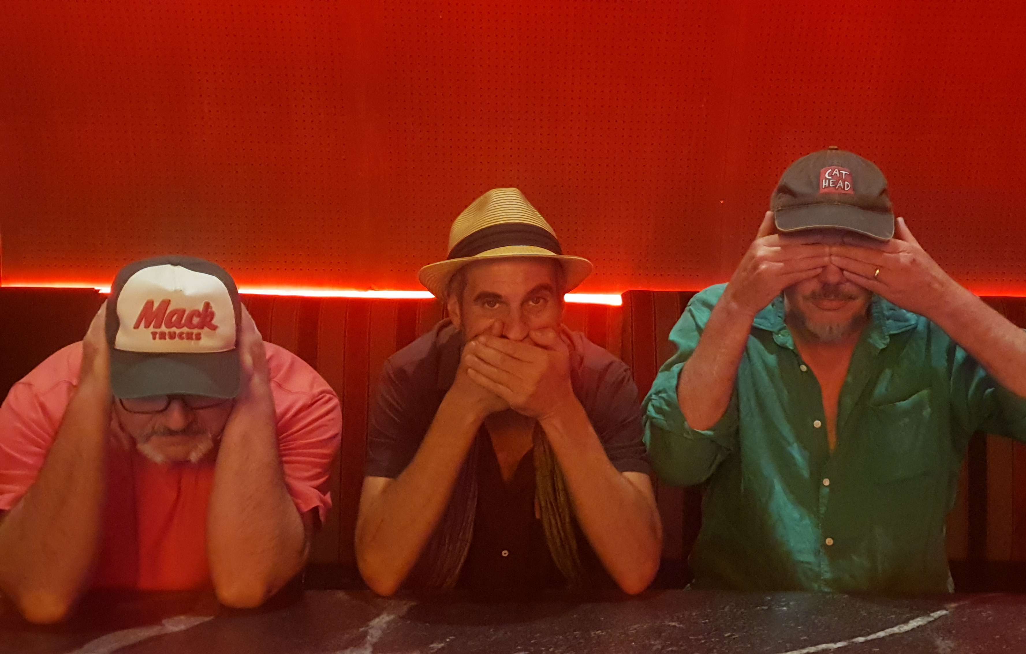 three men with hats covering their eyes while sitting at a table