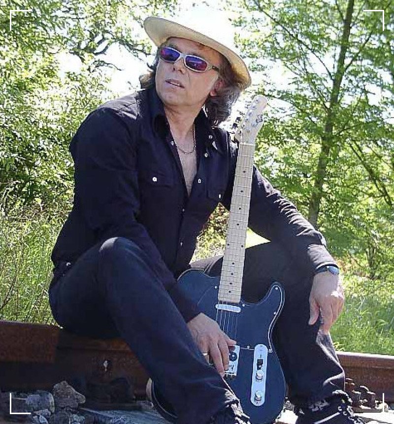 a man in a hat sitting on a train track with a guitar
