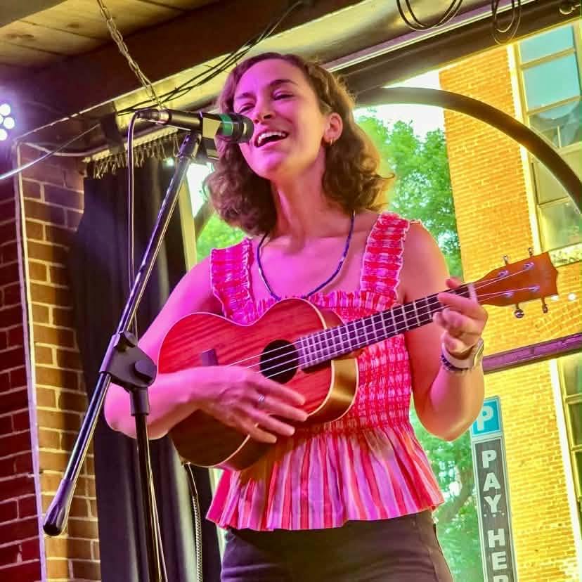 a woman singing into a microphone while playing an ukulele