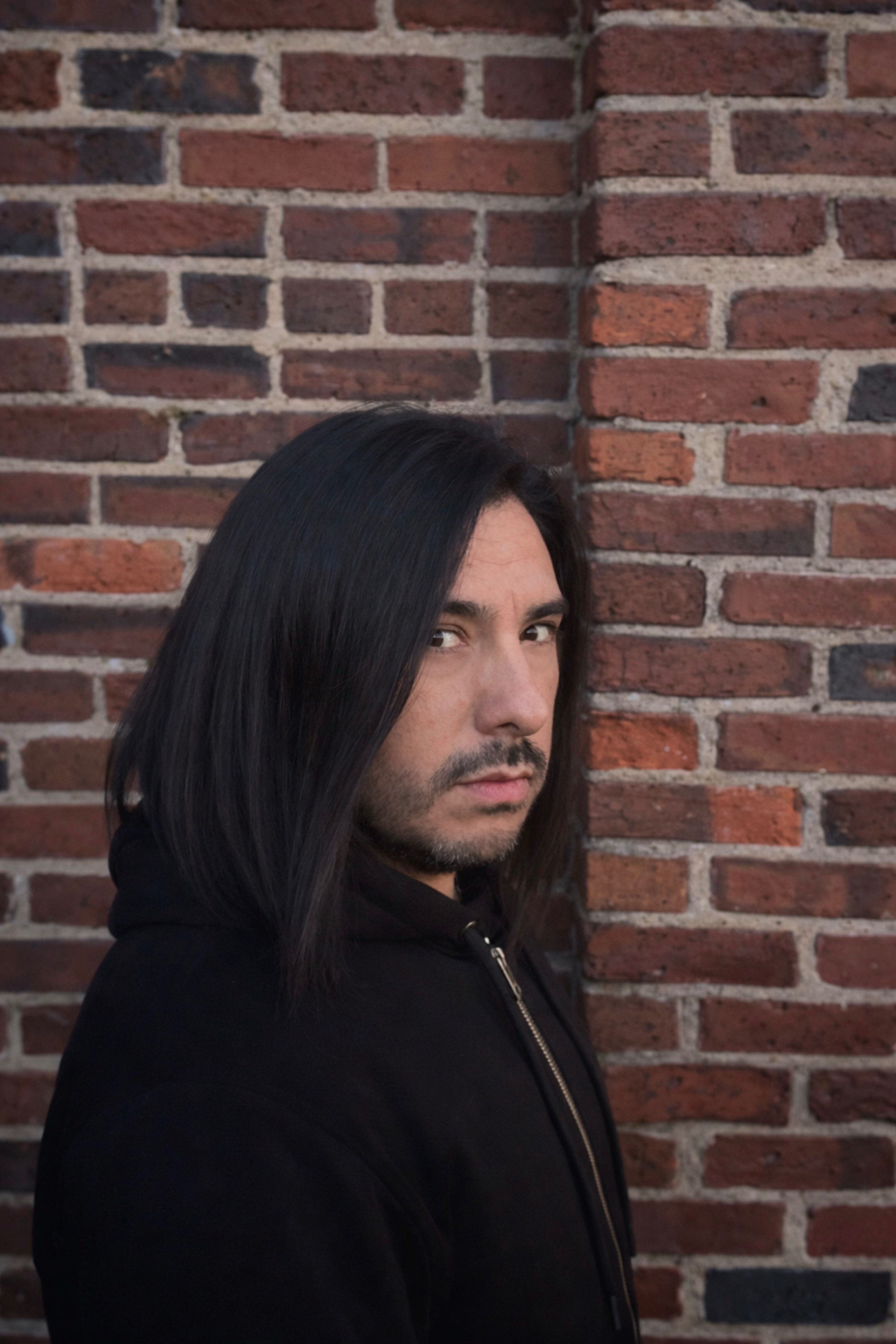 a man with long hair leaning against a brick wall