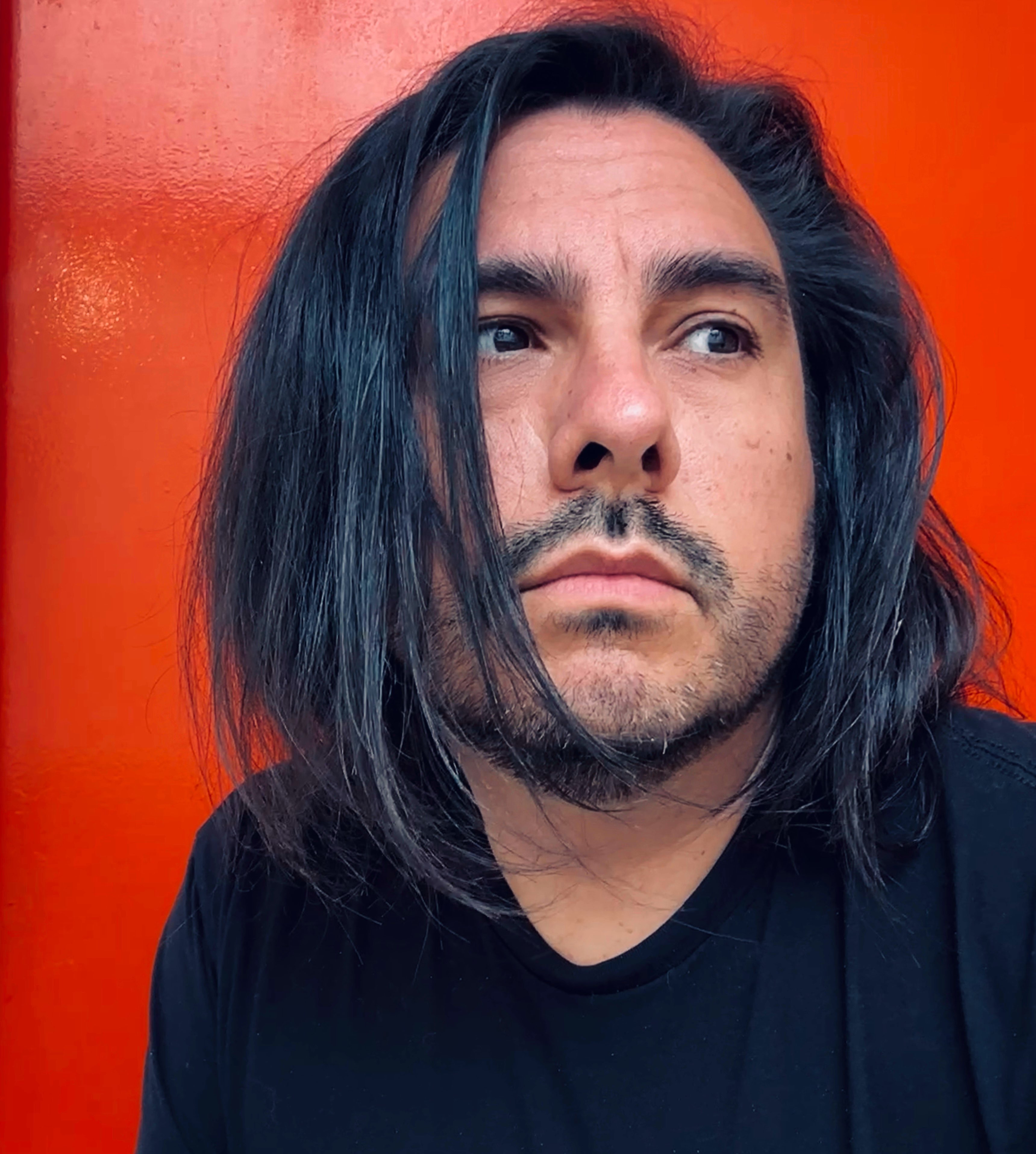 a man with long hair standing in front of an orange wall