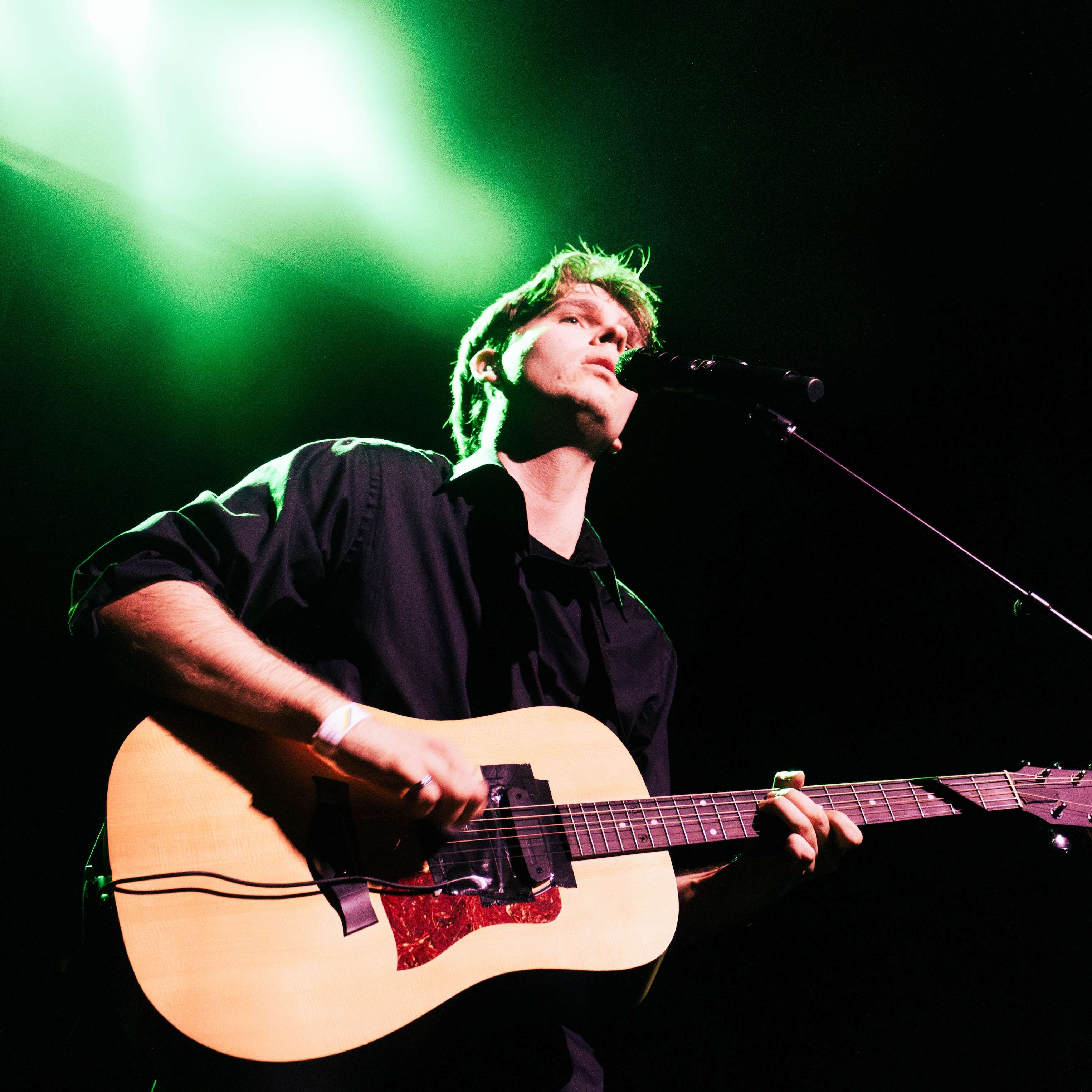 a man playing an acoustic guitar in front of a green light