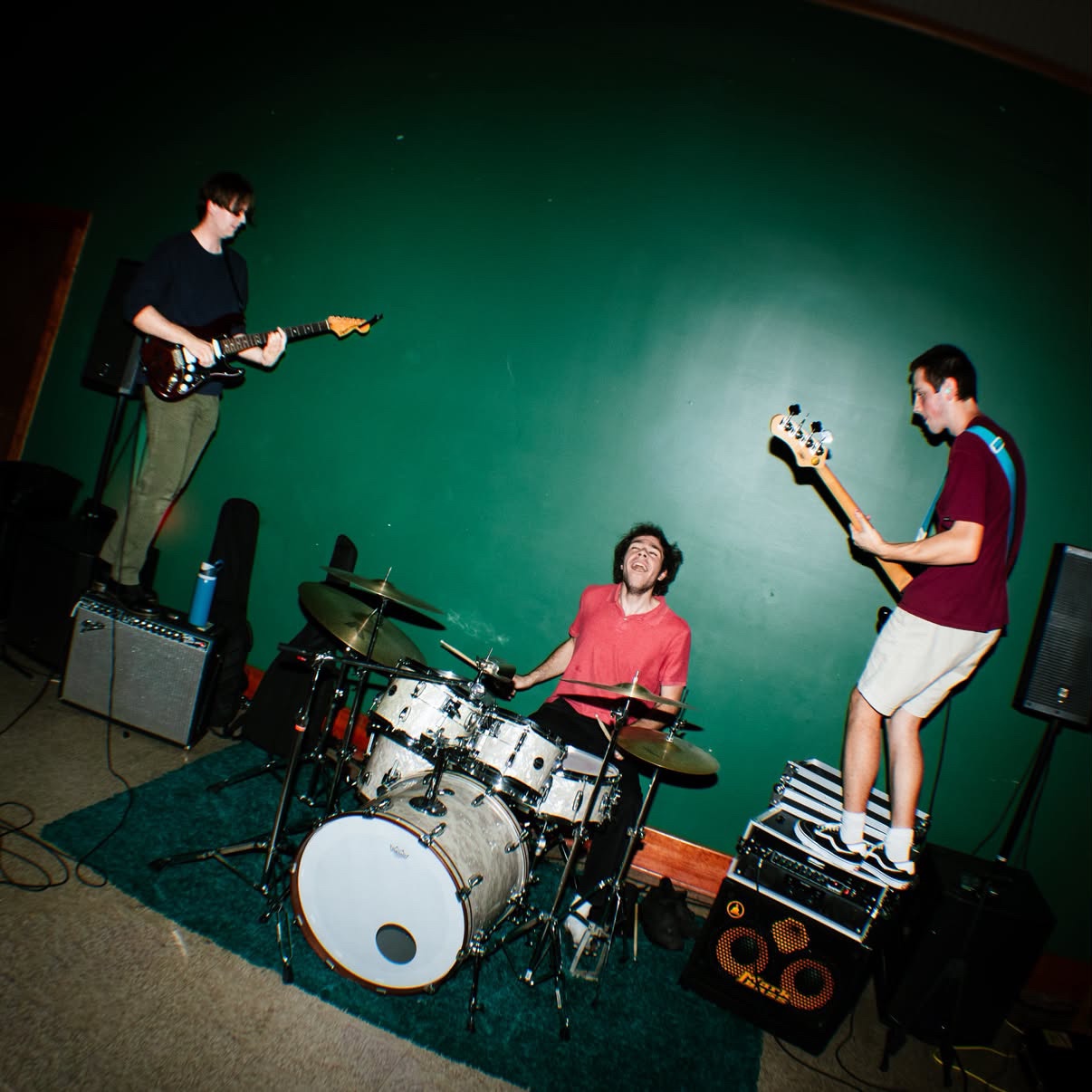 a group of people playing music in a room with a green wall