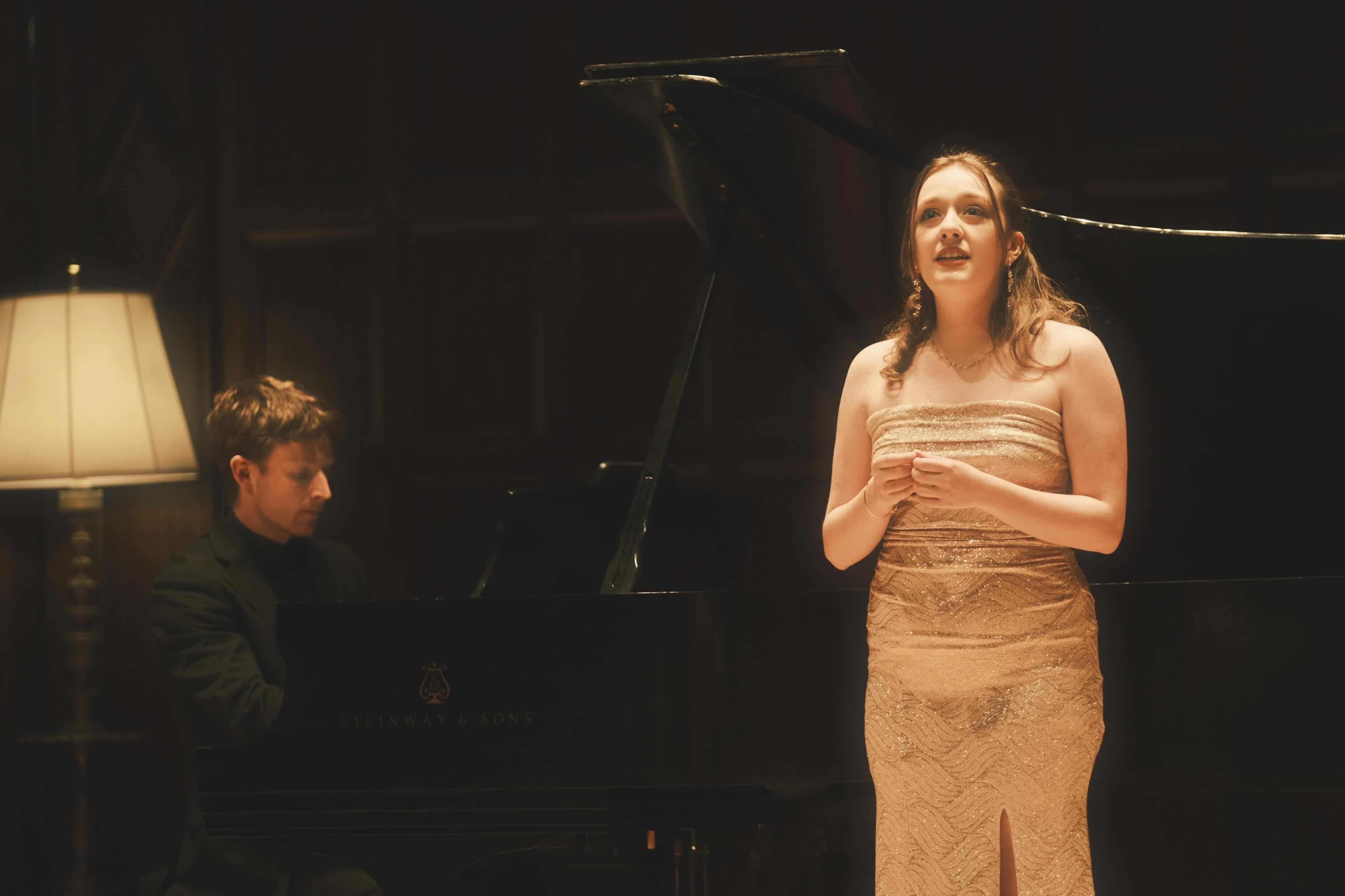 a woman in a dress standing next to a piano