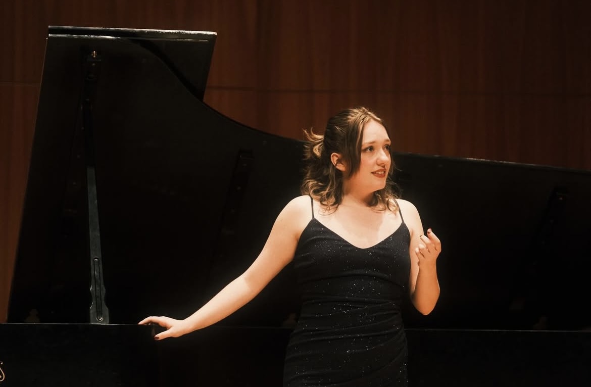 a woman in a black dress standing in front of a piano