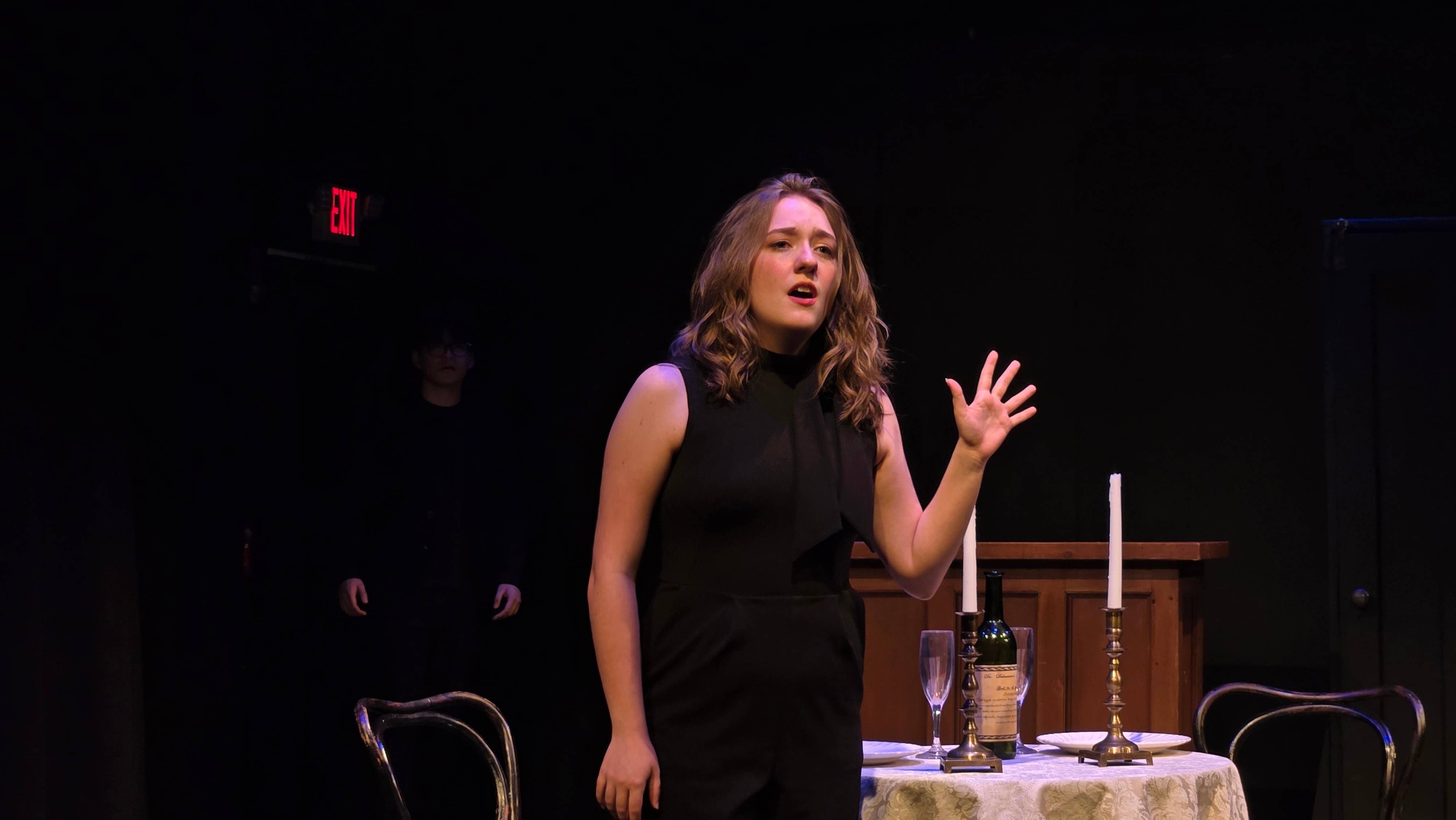 a woman in a black dress is standing in front of a table