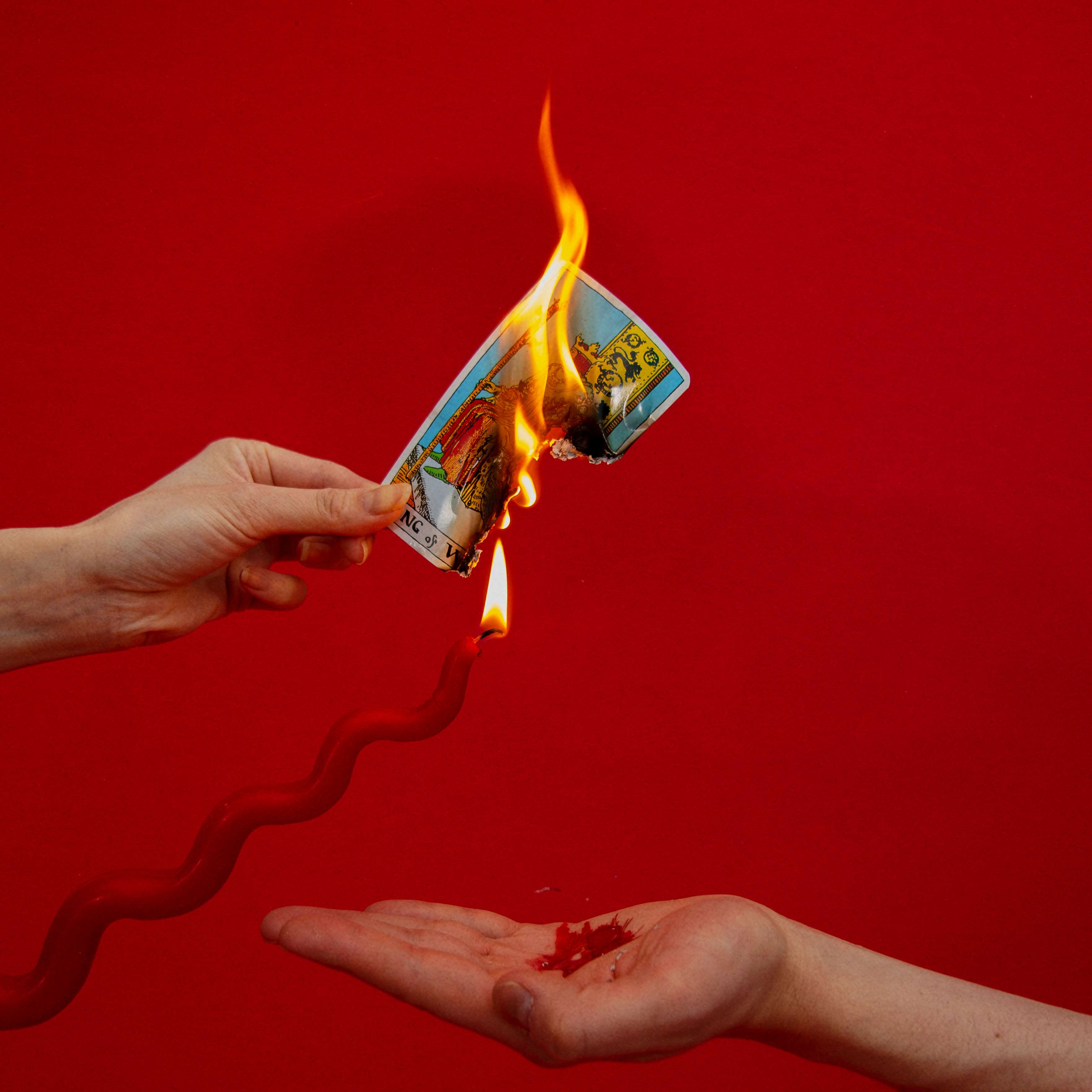 a pair of hands holding a burning card on a red background