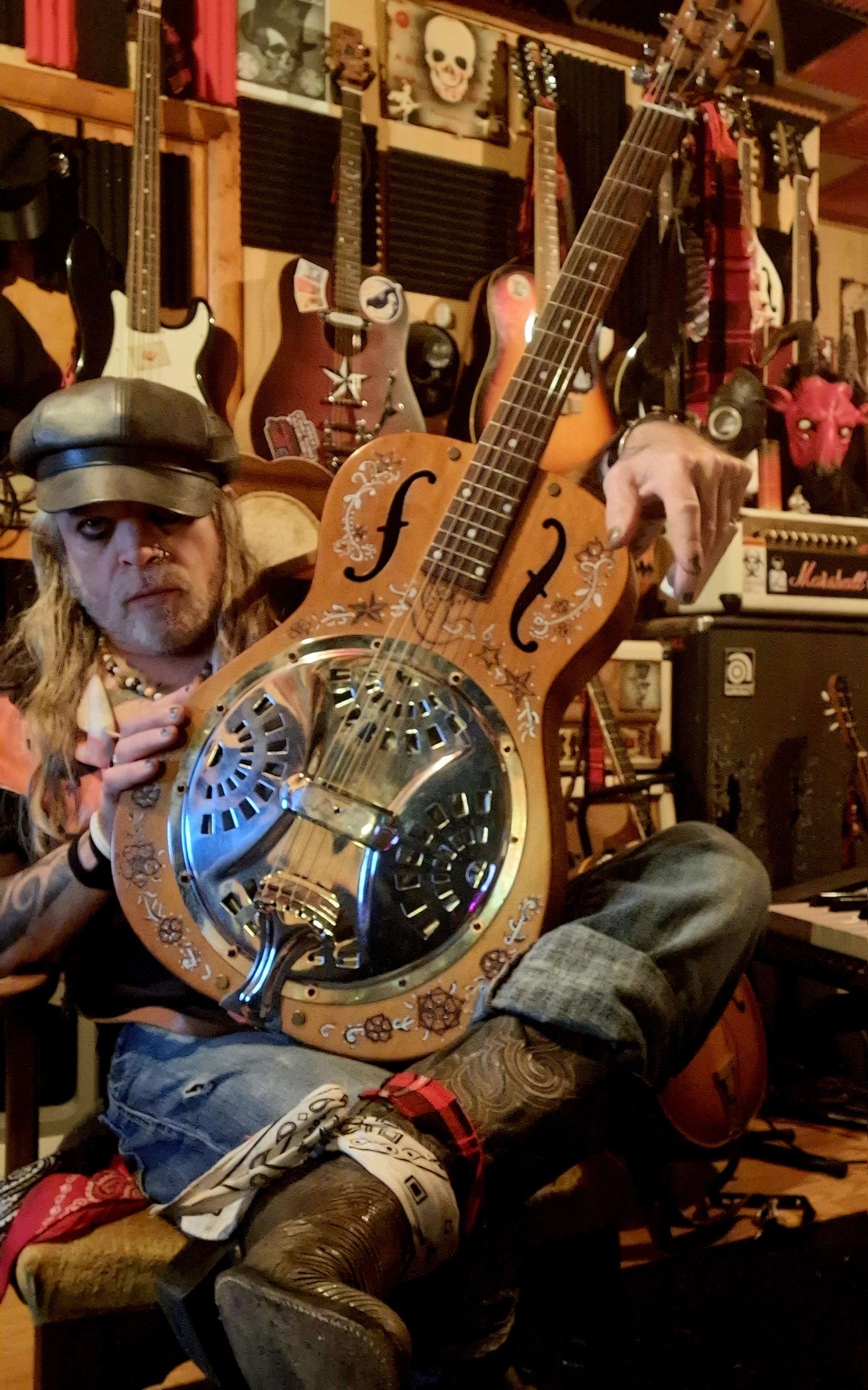 a man holding a resonator guitar in a room full of guitars