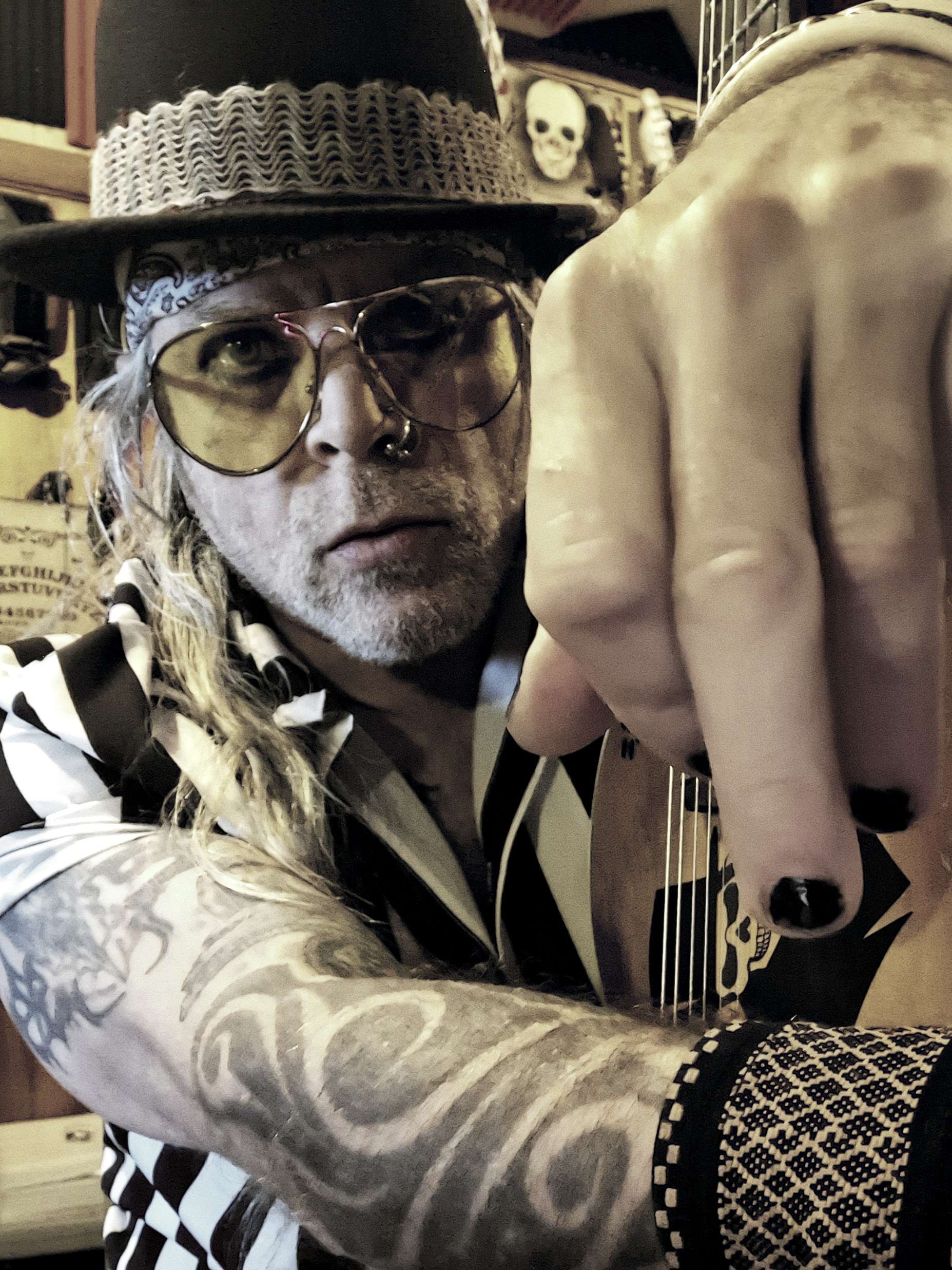 a man with tattoos and a hat is holding a guitar