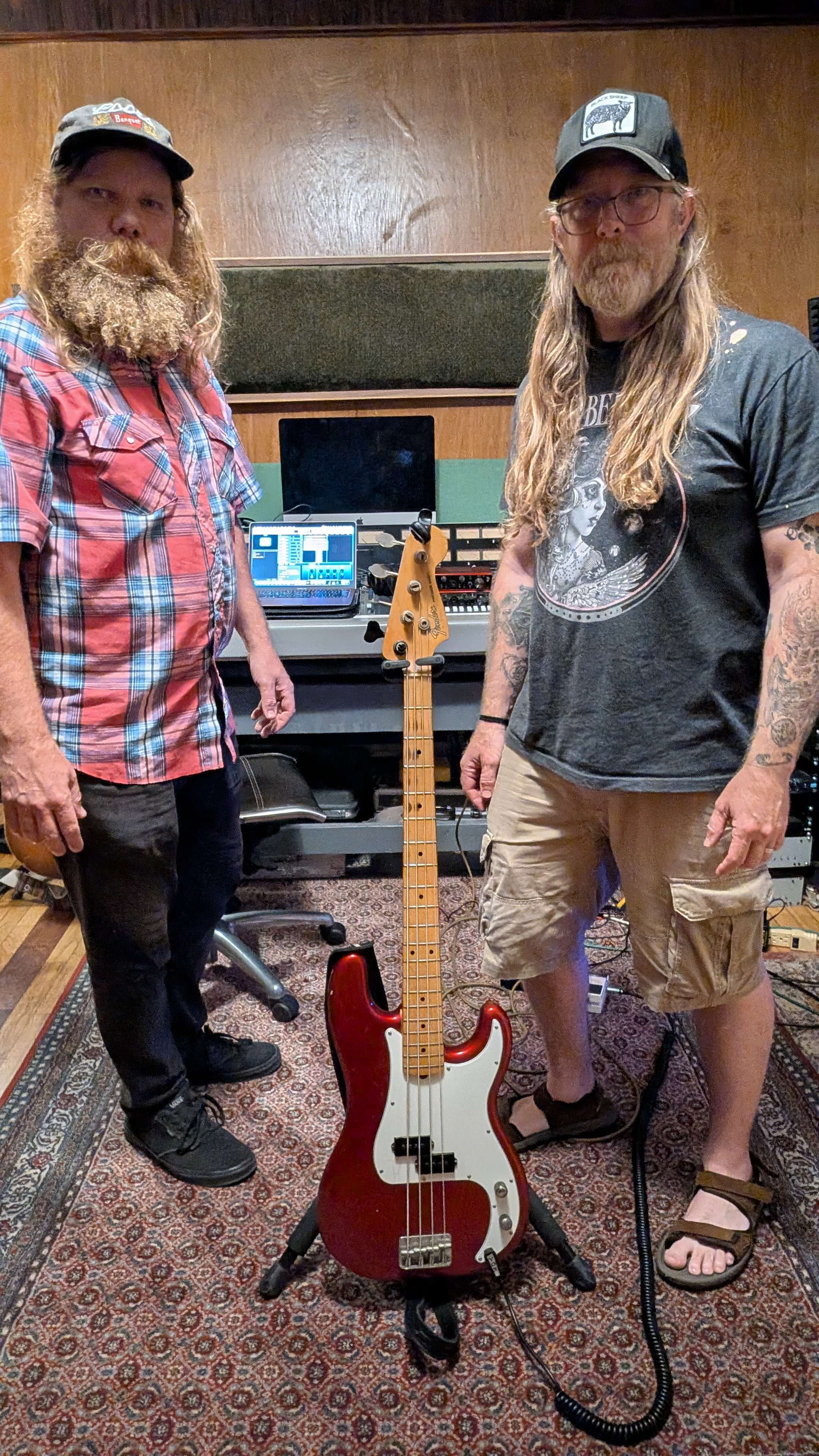 two men standing next to a guitar in a recording studio