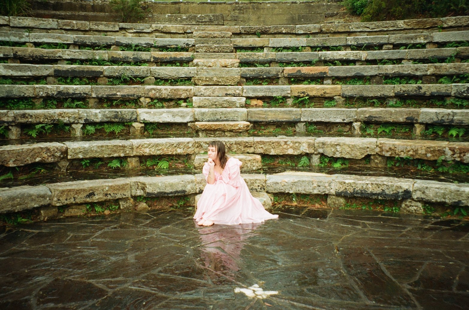 a woman in a pink dress sitting on the steps of an amphitheater