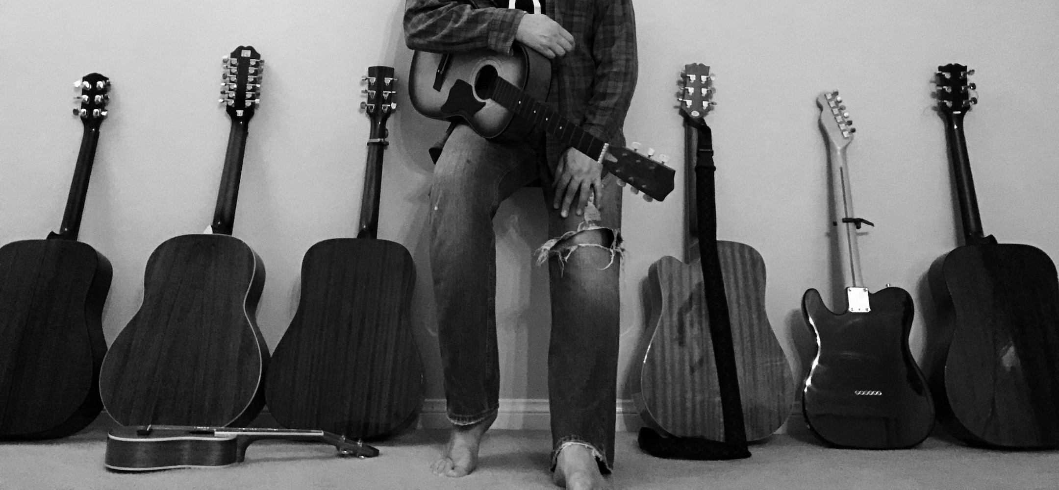 a man leaning against a wall full of guitars
