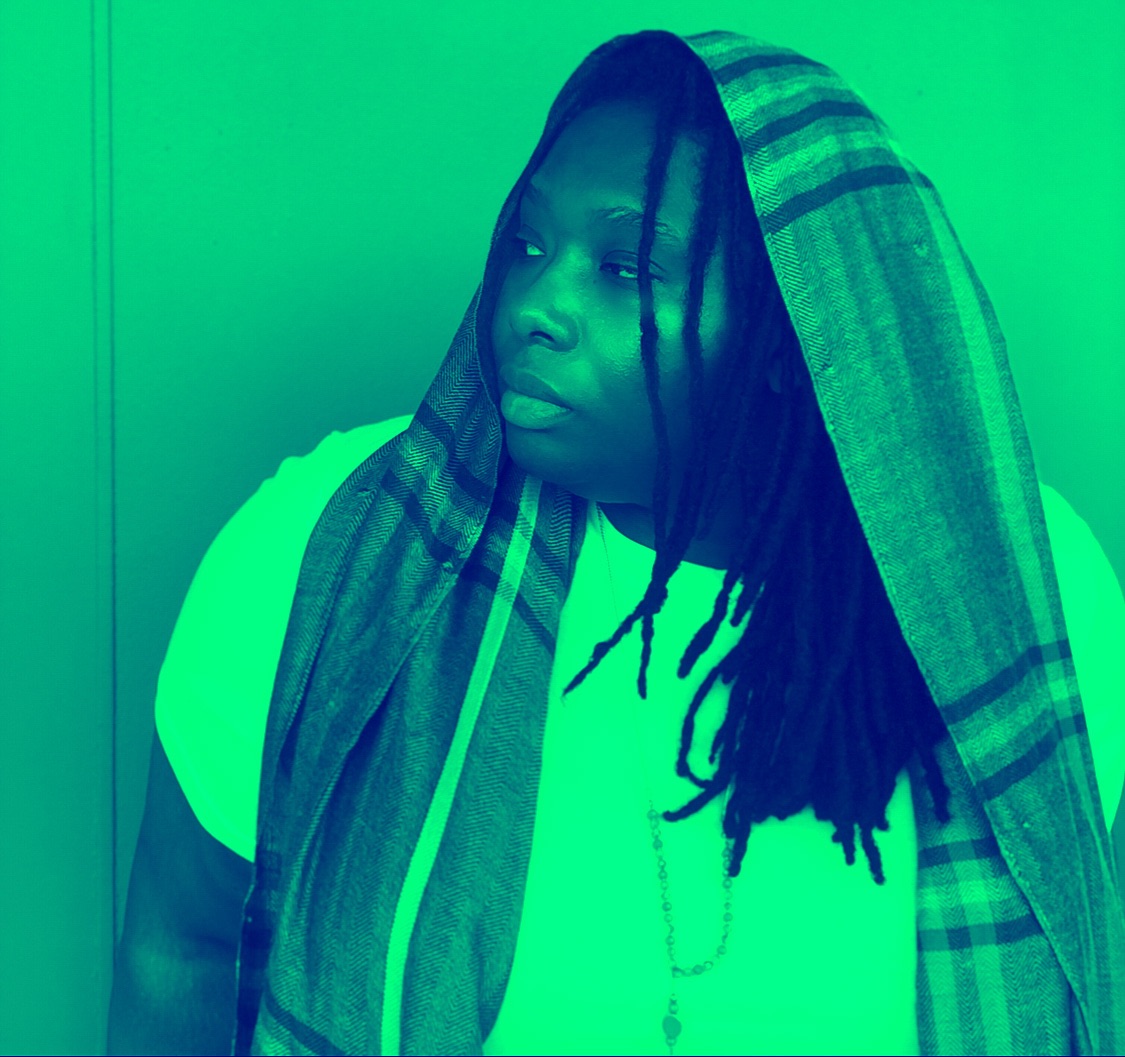a woman with dreadlocks and a scarf in front of a green wall