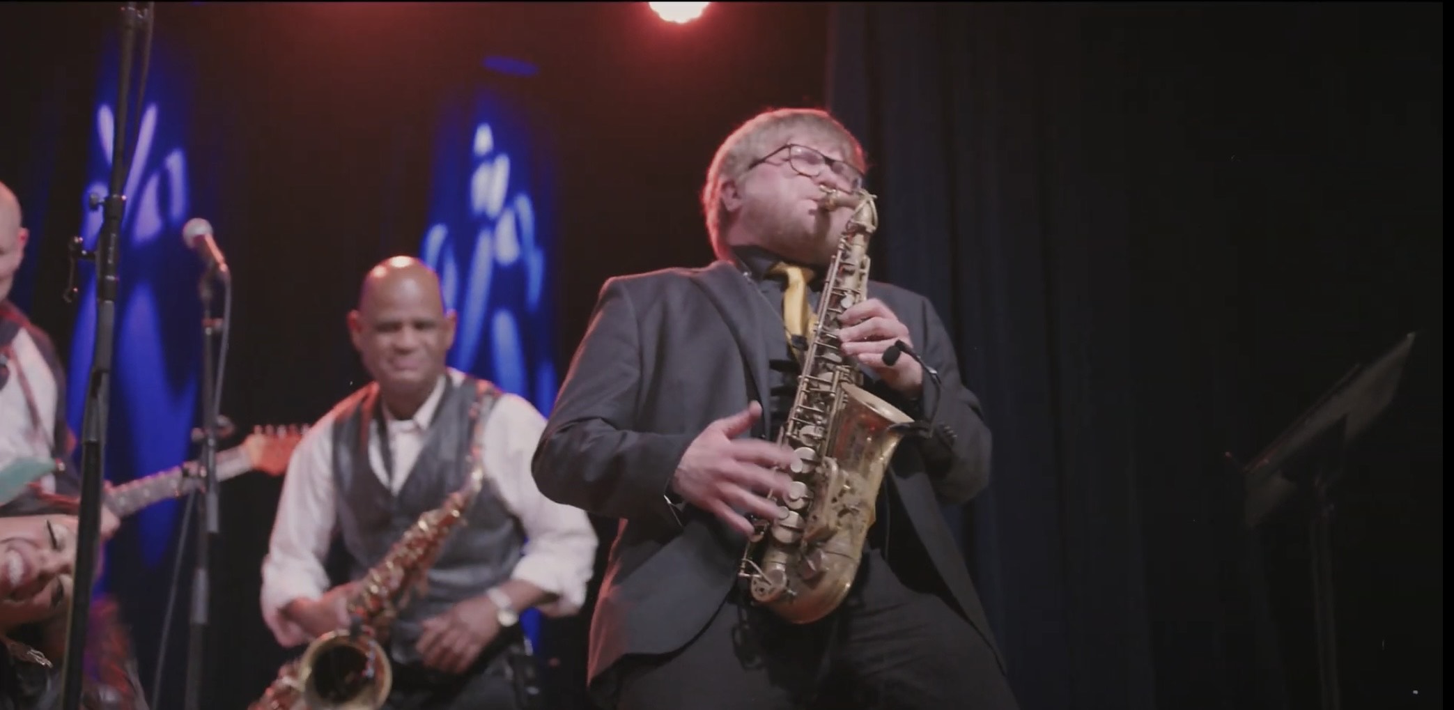a man playing a saxophone on stage with other musicians