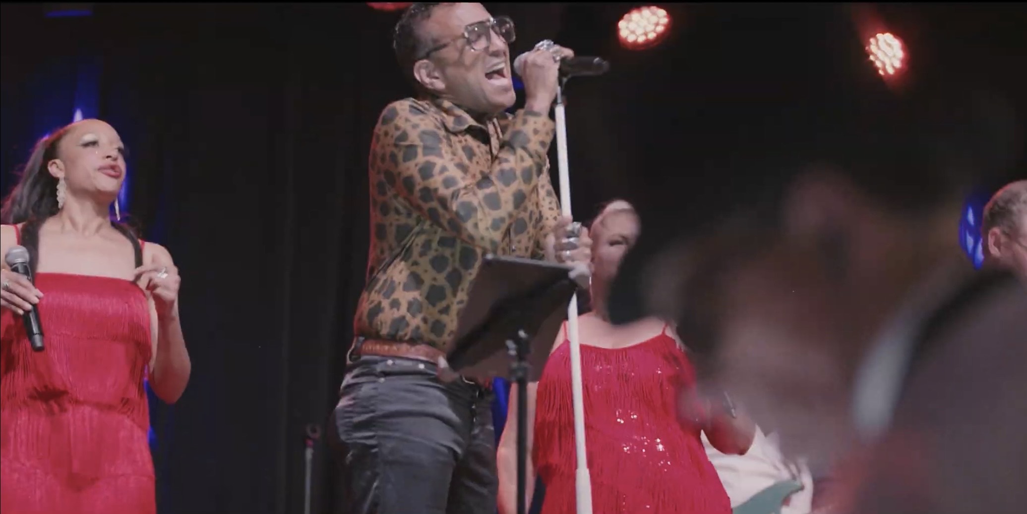 a man in a red dress singing into a microphone