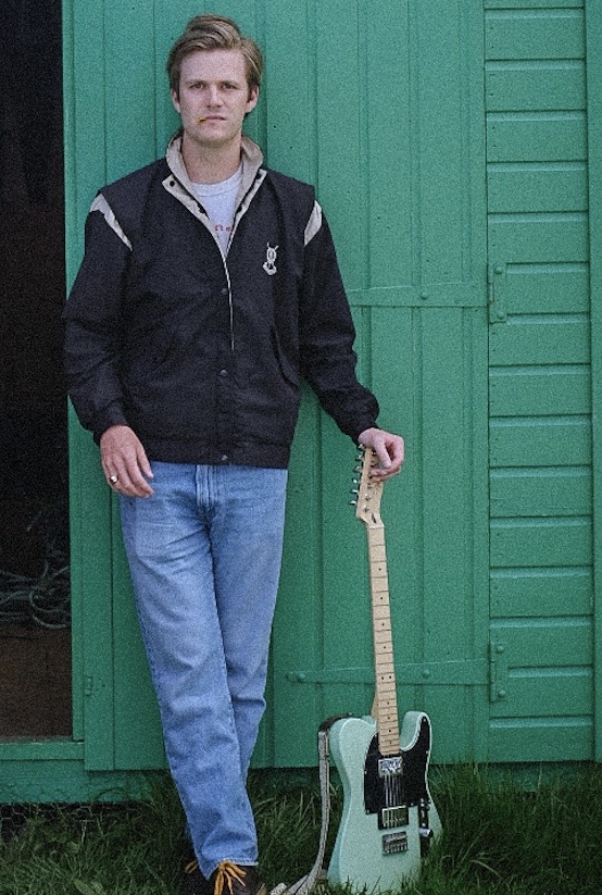 a man standing in front of a green shed with a guitar