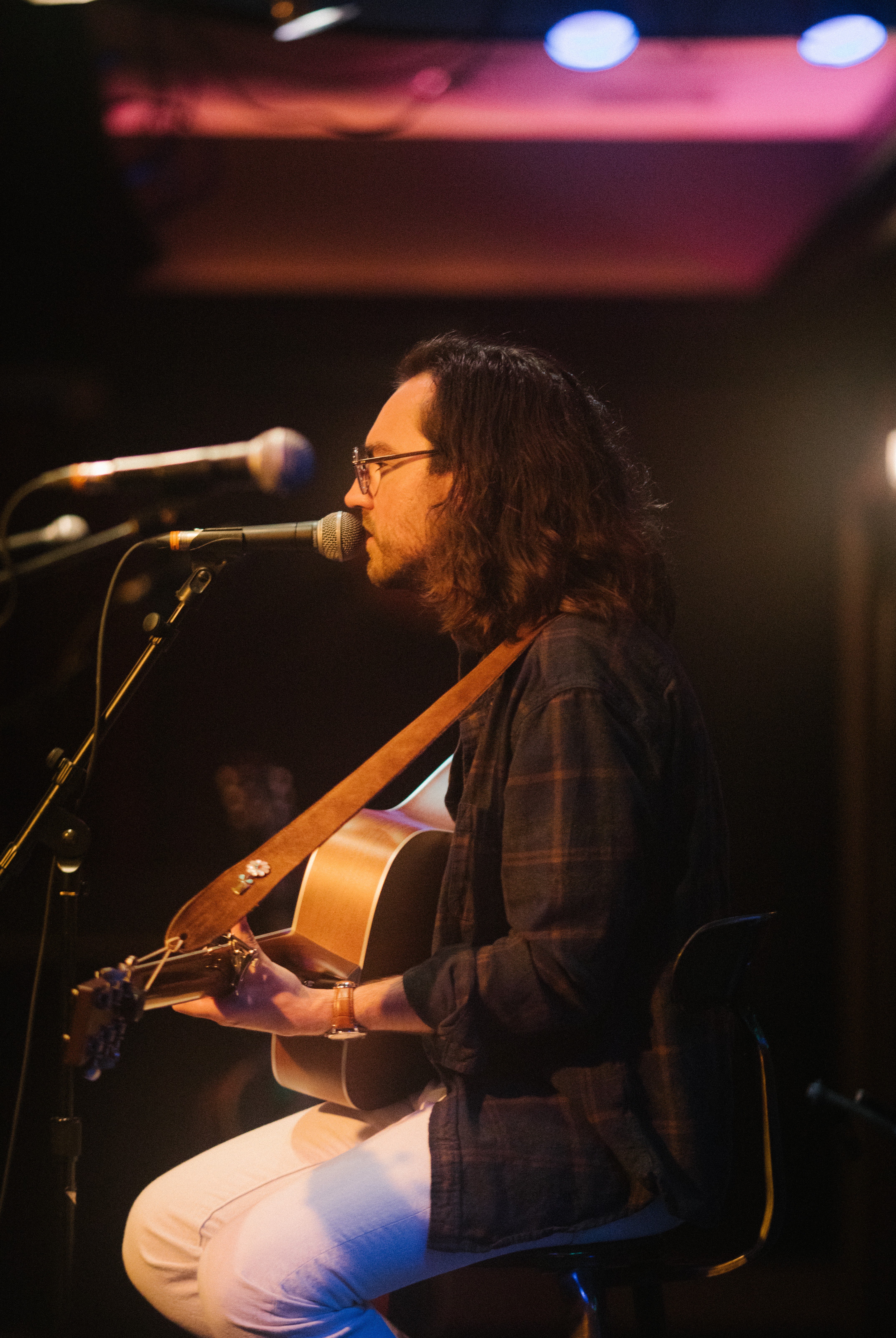 a man playing an acoustic guitar in front of microphones