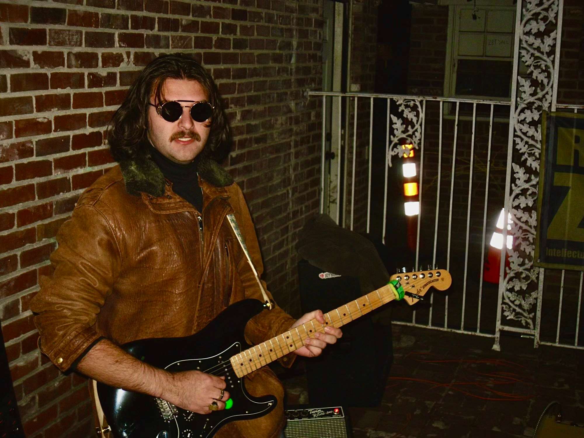 a man holding a guitar in front of a brick wall
