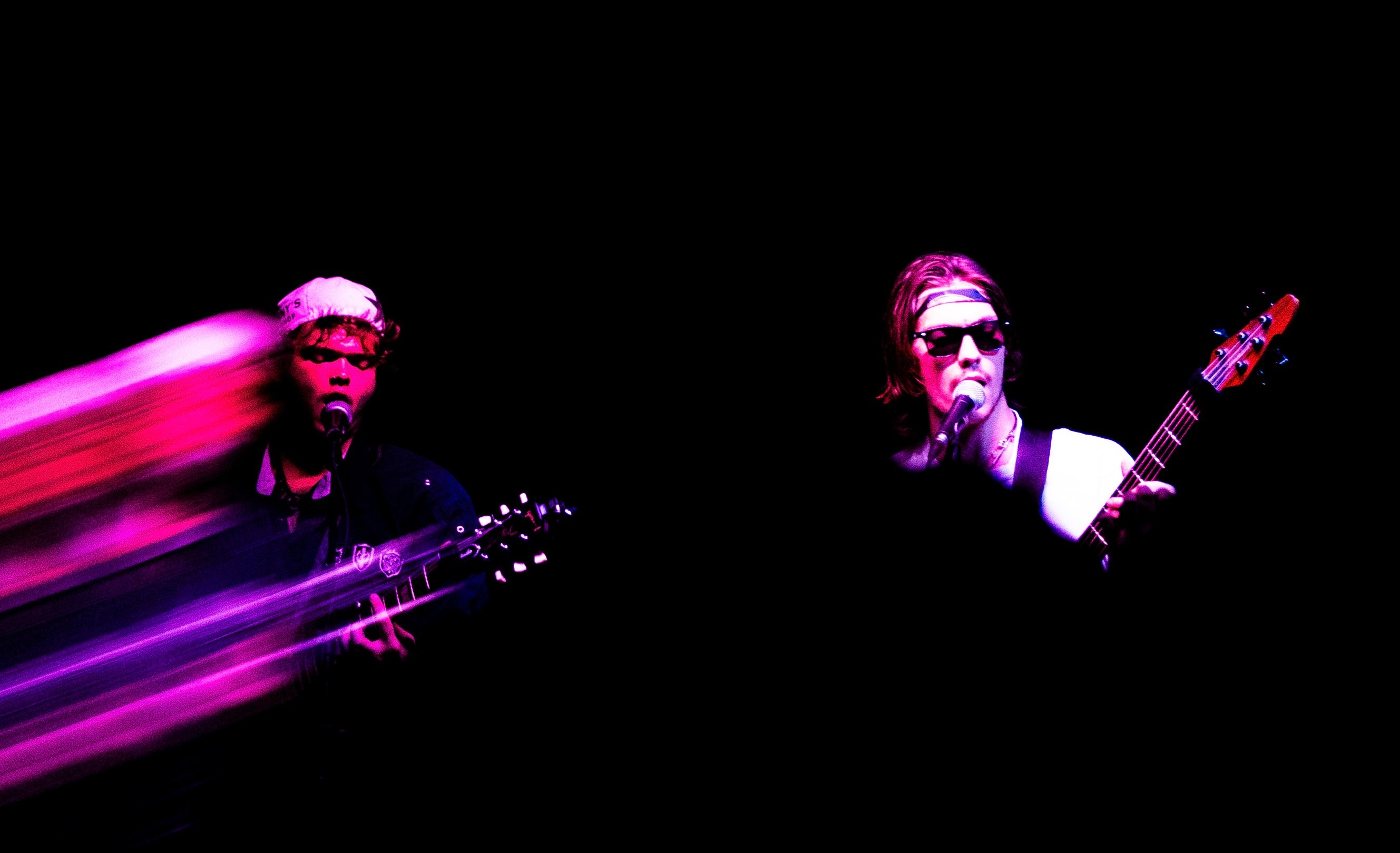 two men playing guitars in a dark room