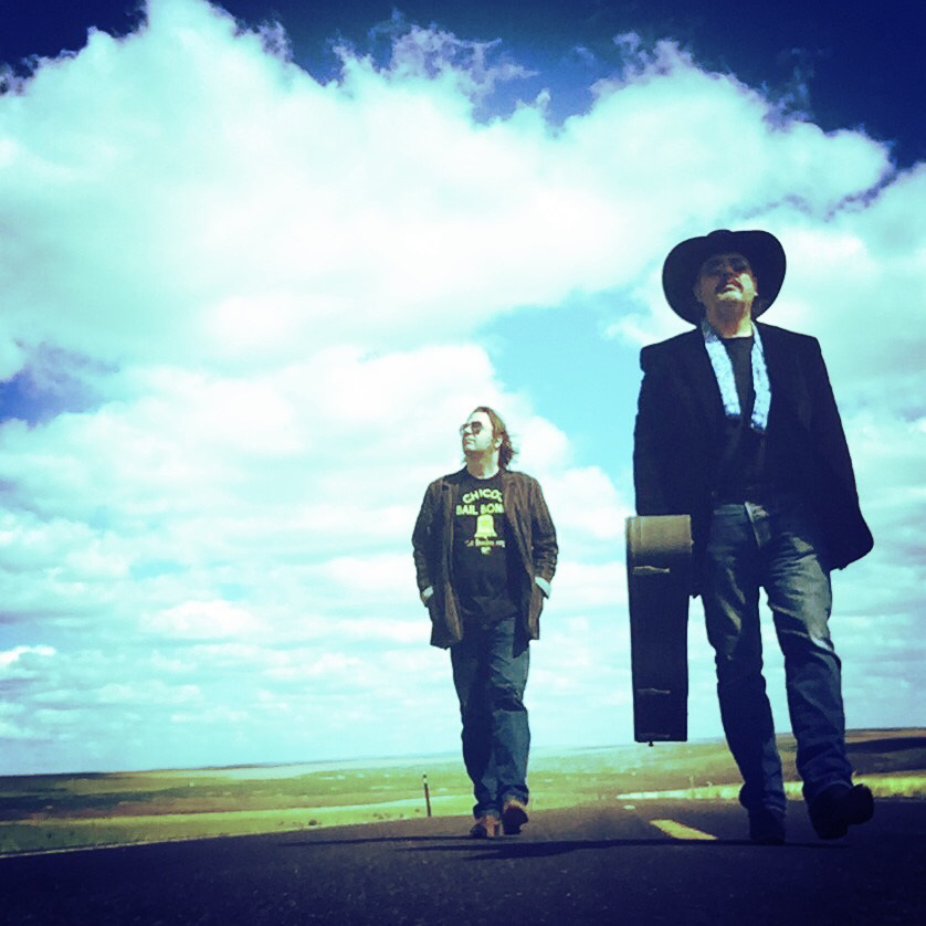 two men walking down a road with a cowboy hat on