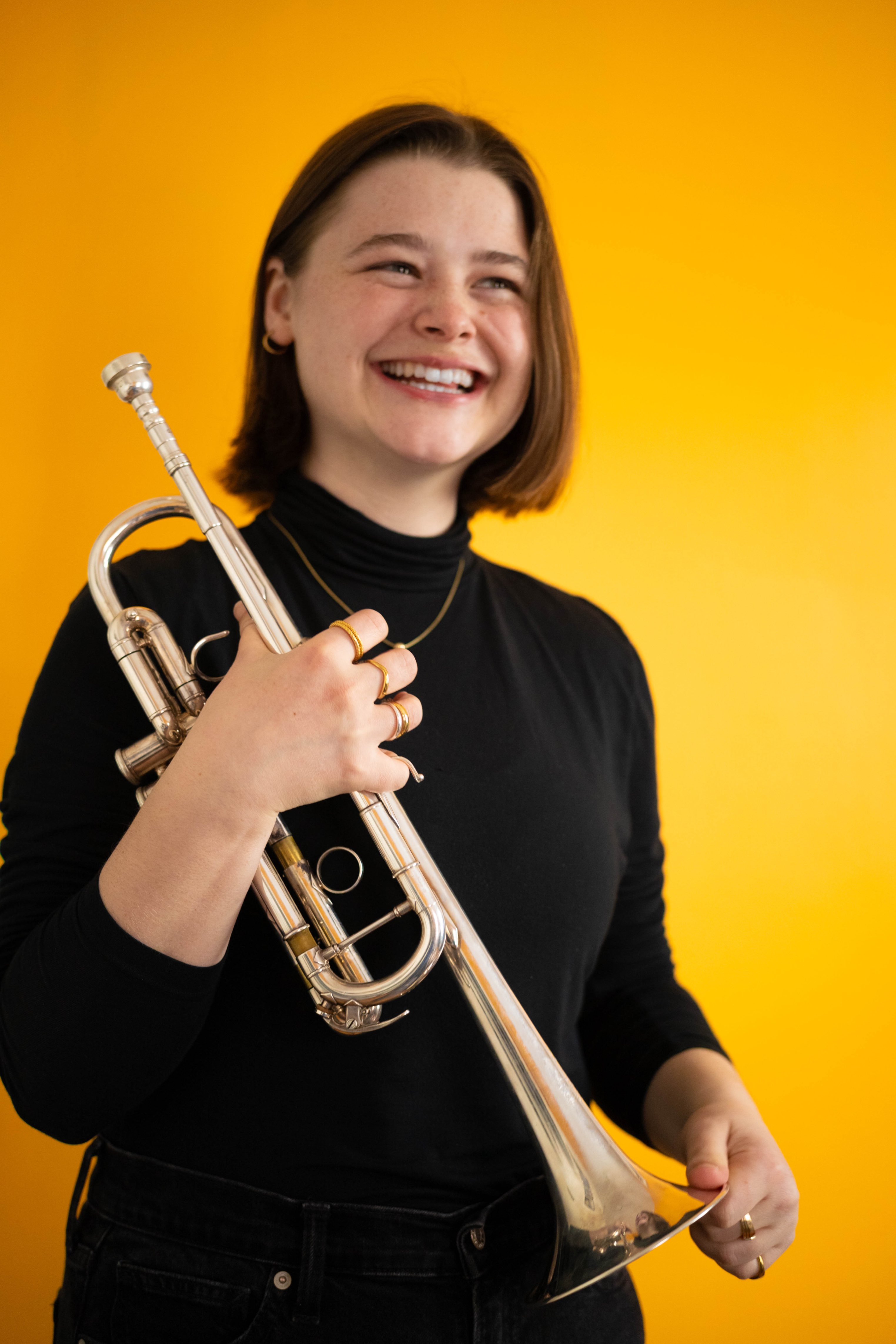 a woman holding a trumpet in front of a yellow background