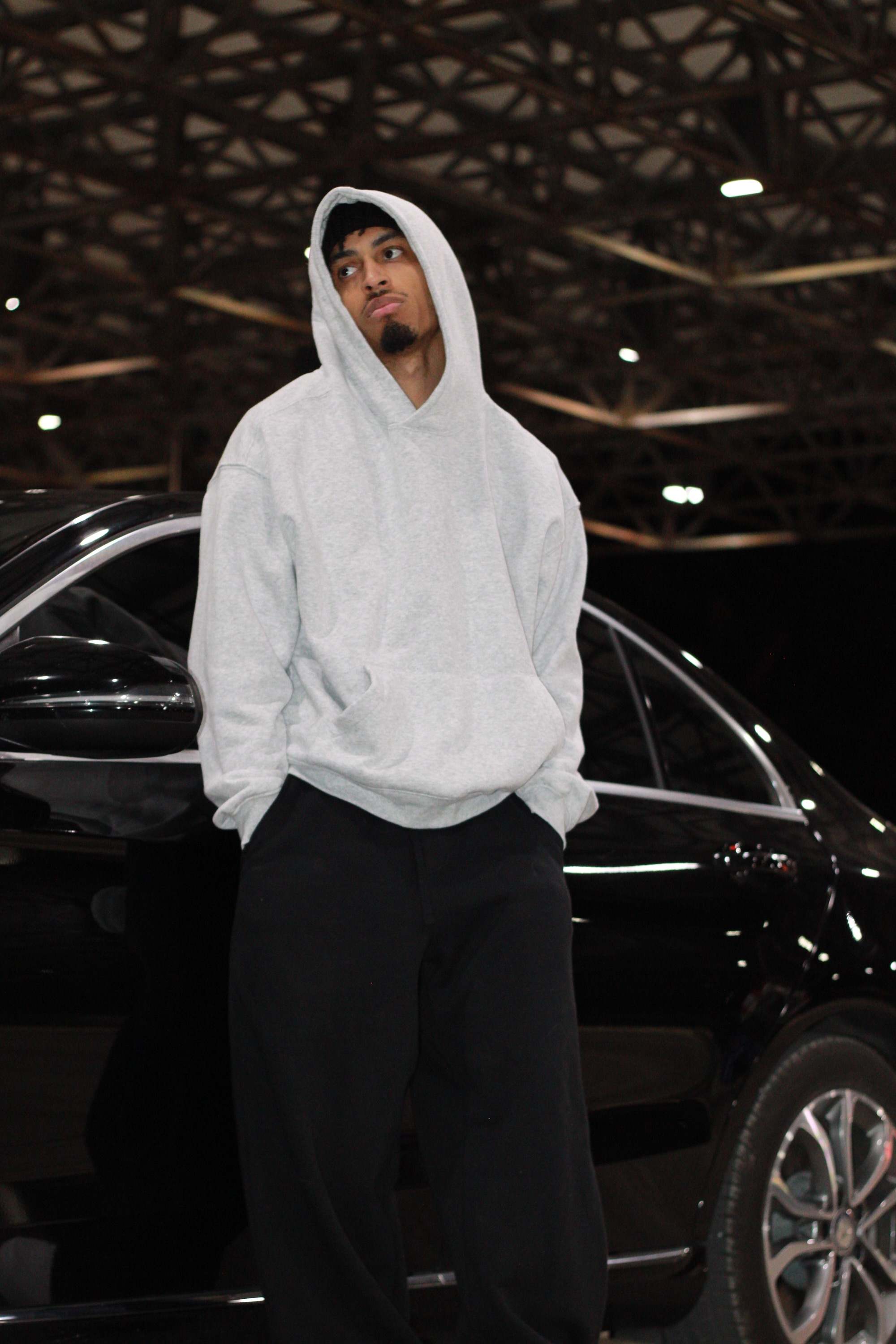 a man in a hoodie standing next to a black car