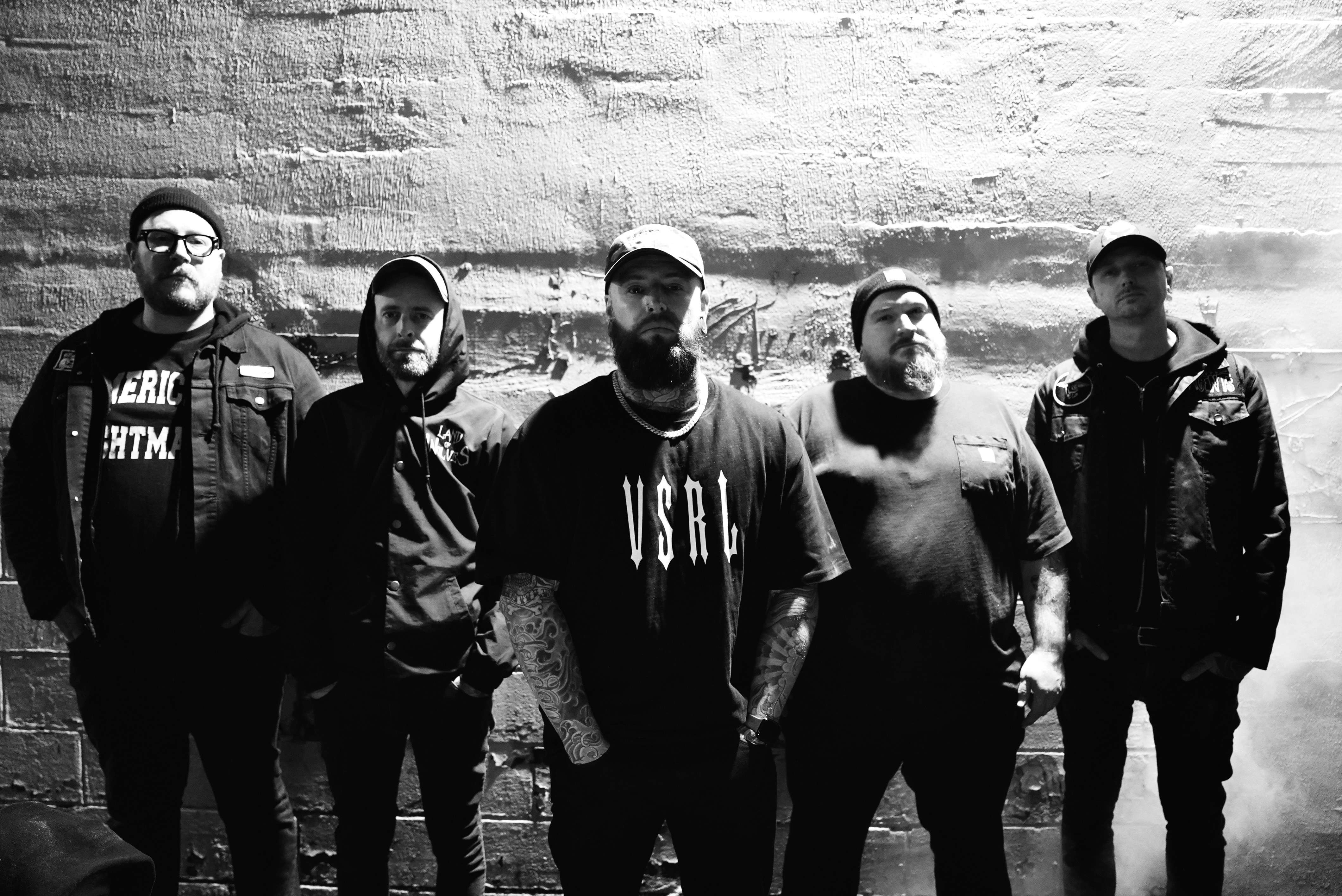 a black and white photo of a group of men standing in front of a brick wall