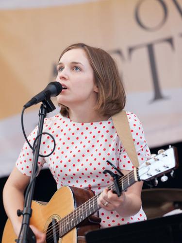 a woman singing into a microphone with an acoustic guitar