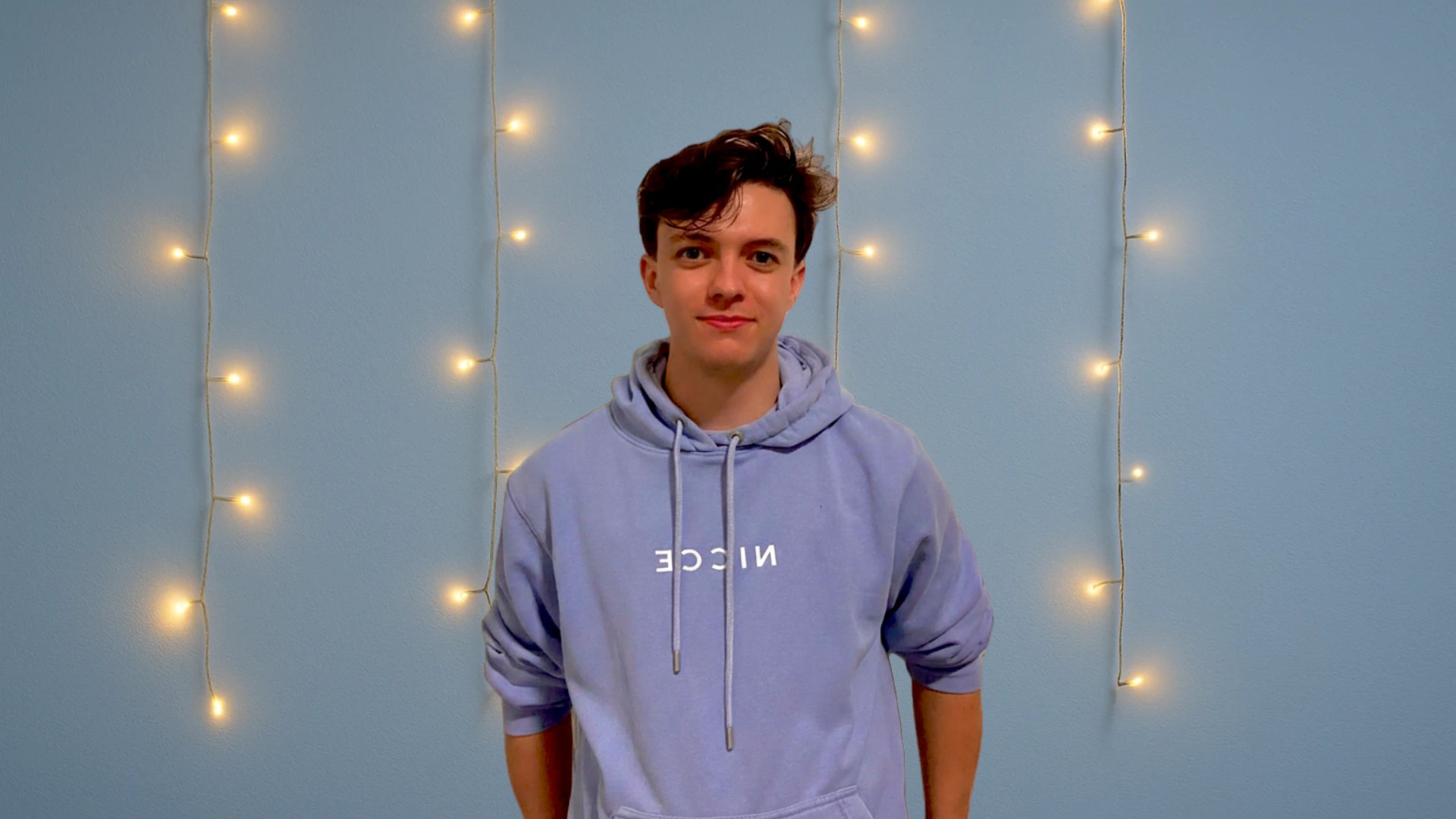 a young man in a blue hoodie standing in front of lights