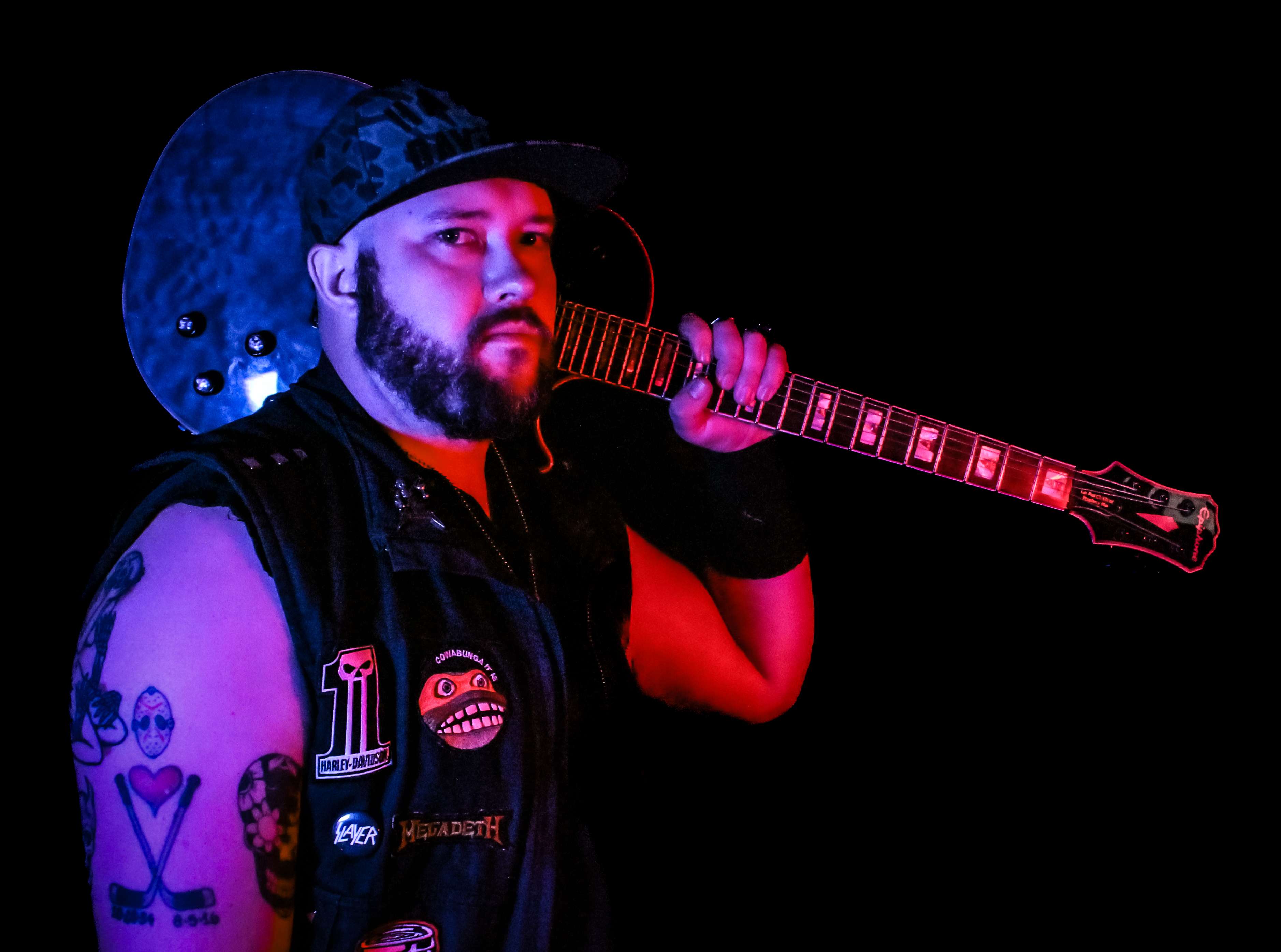 a man with tattoos holding a guitar in front of a dark background