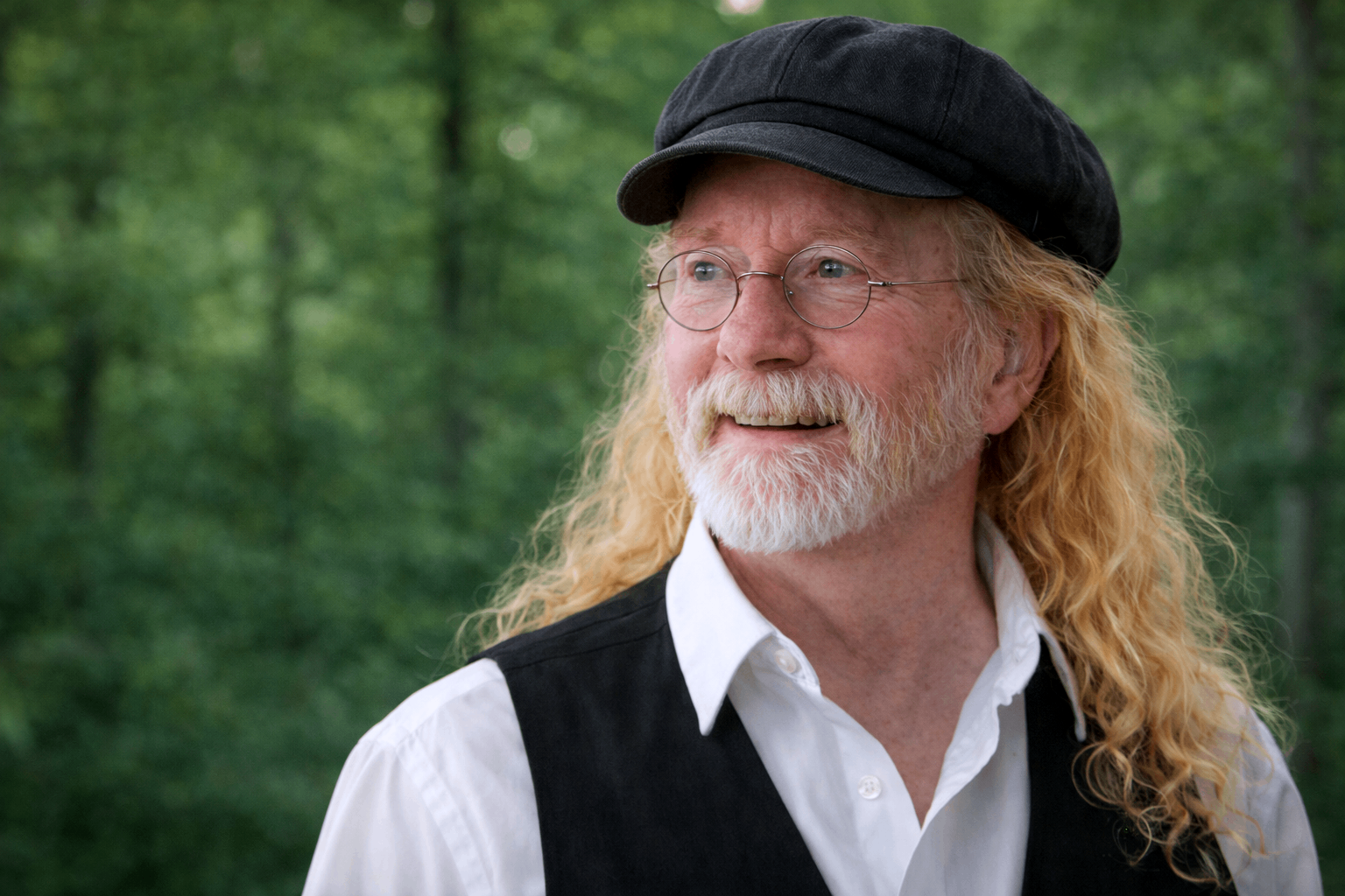 a man with a beard and long hair wearing a vest and hat