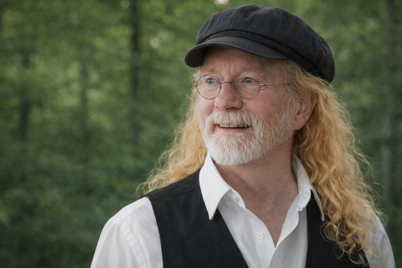 a man with a beard and long hair wearing a vest and hat