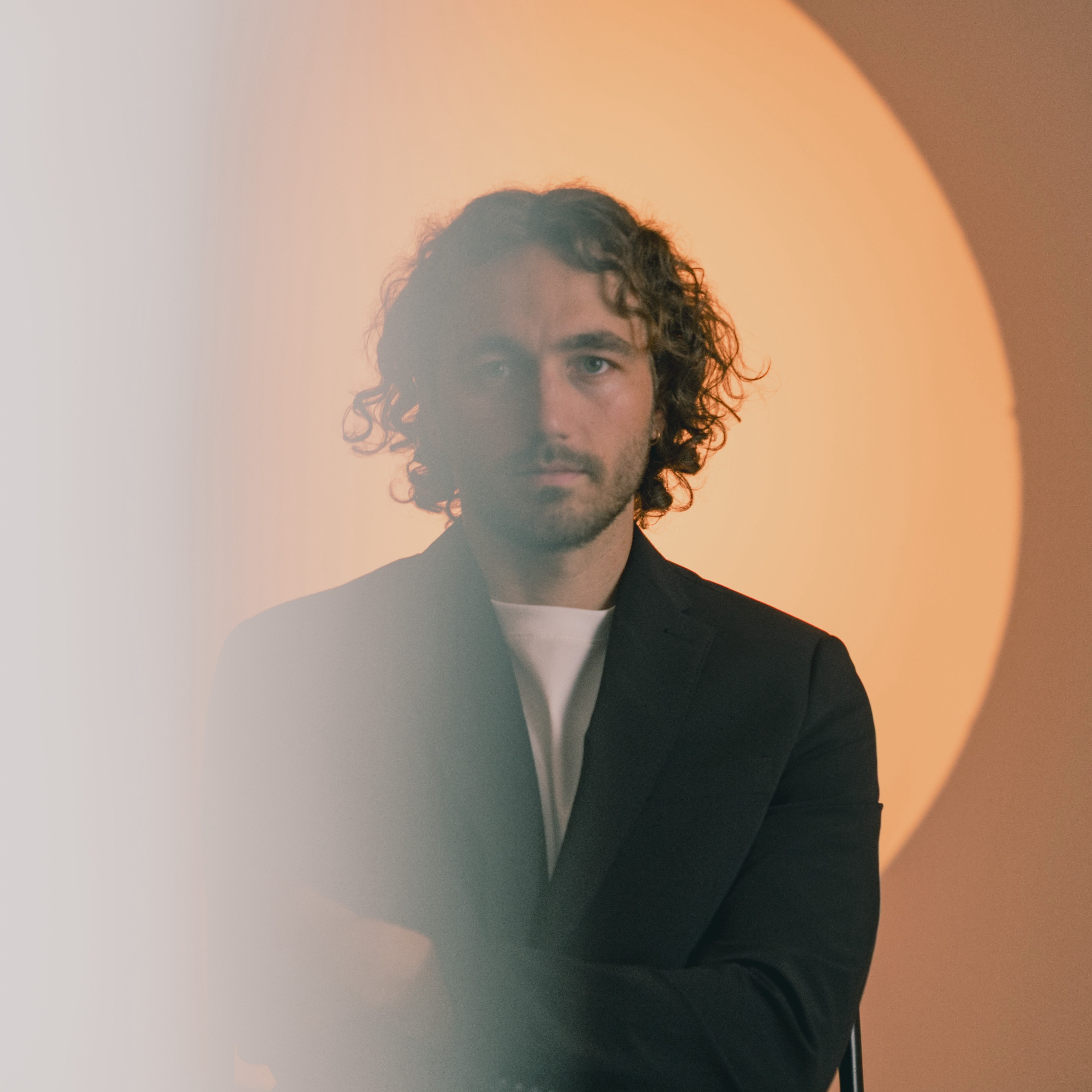 a man with curly hair standing in front of a circular light