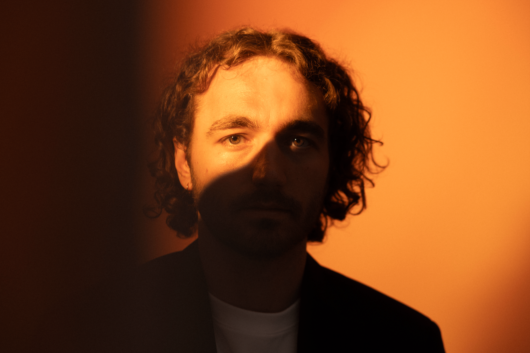Ryan Delmonico - Trials and Pains - EP: a man with curly hair standing in front of an orange wall