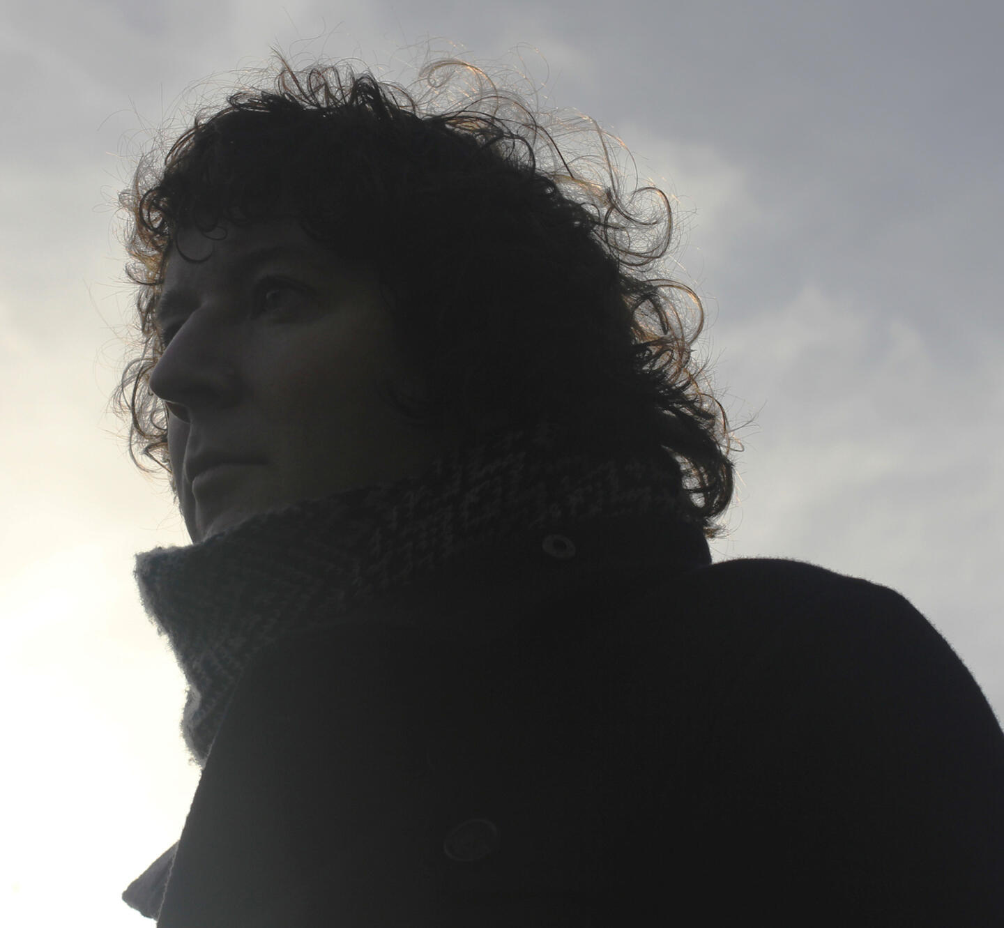 a man with curly hair standing in front of a cloudy sky