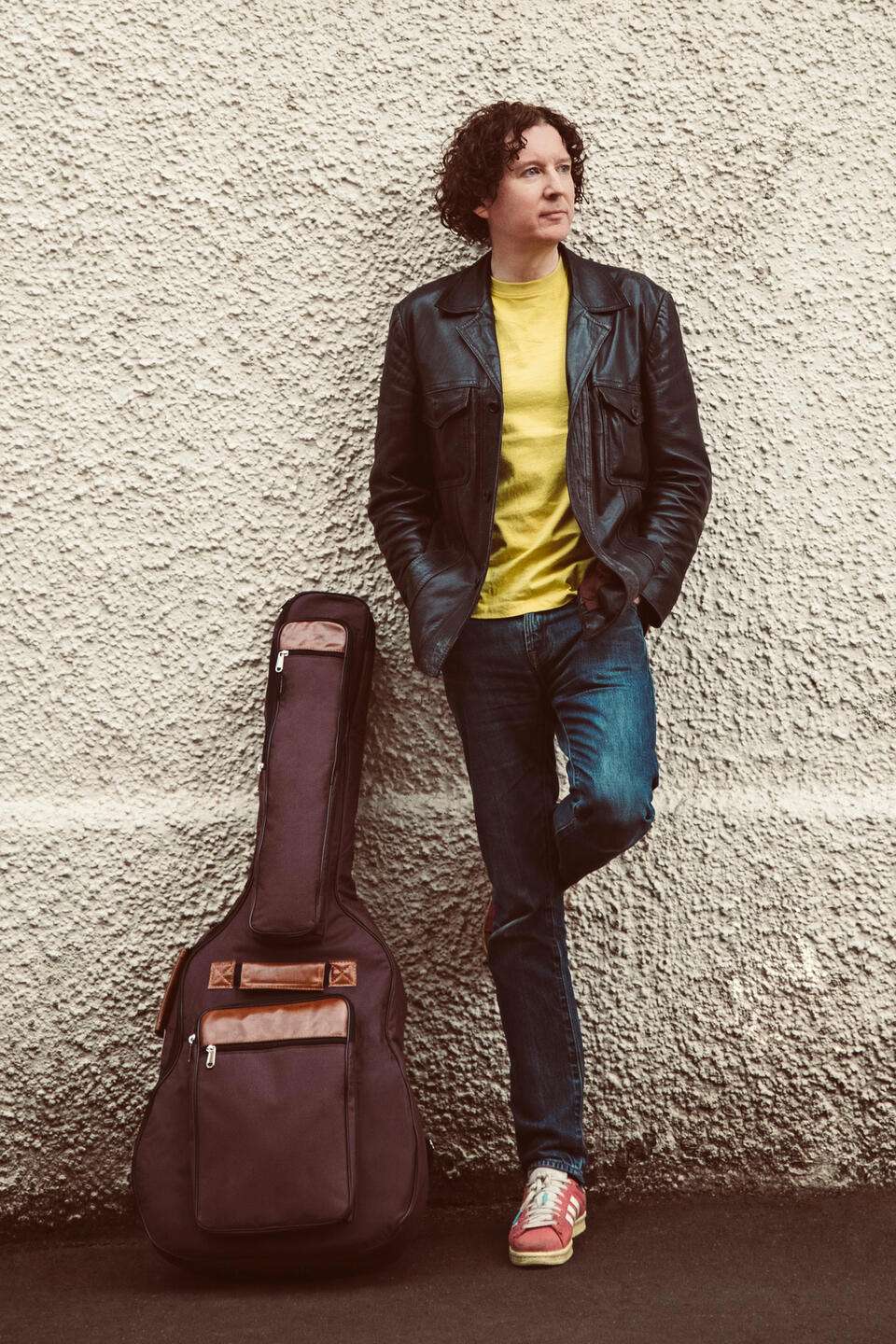a young man leaning against a wall with an acoustic guitar