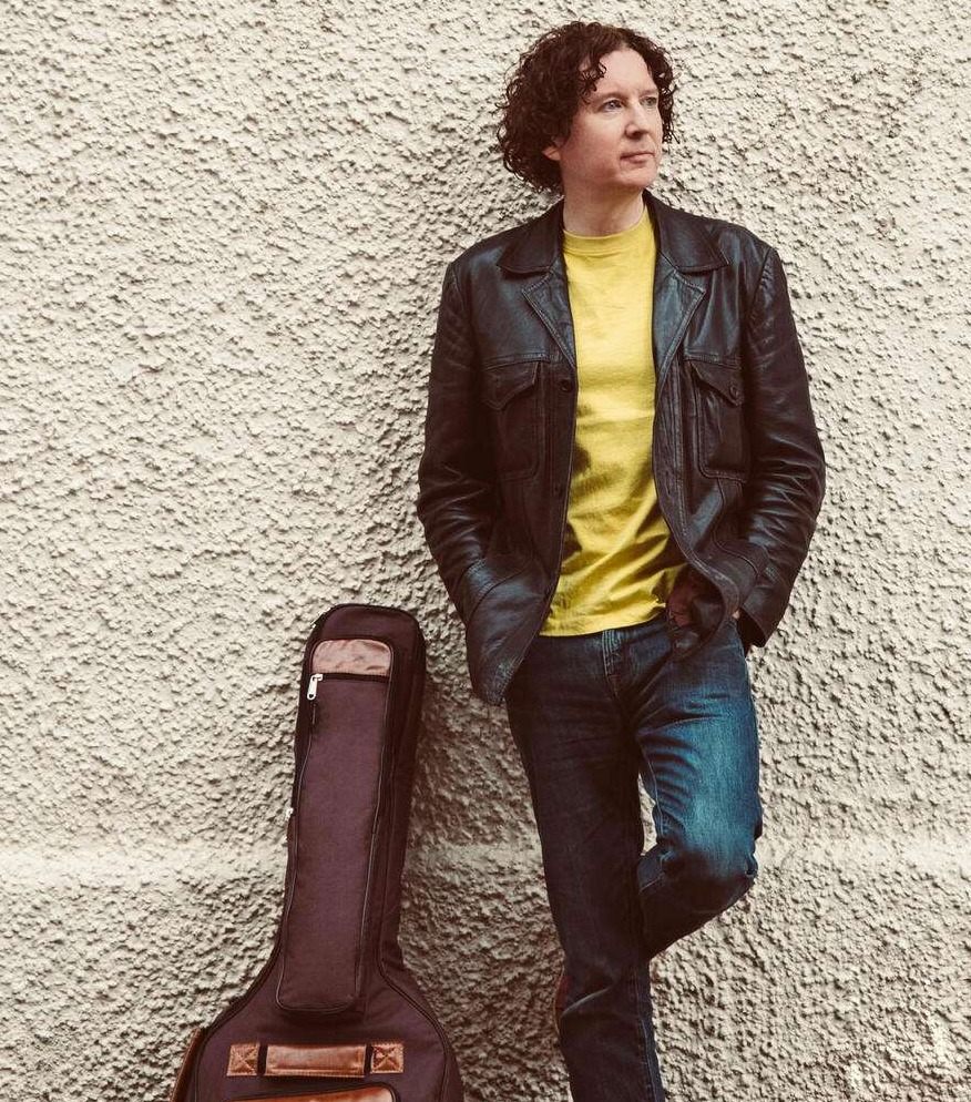 a man leaning against a wall with an acoustic guitar