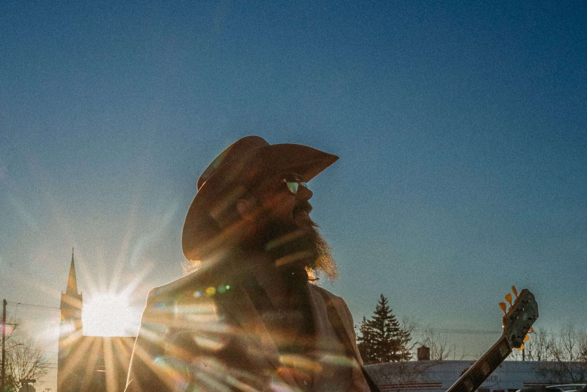 a man in a cowboy hat holding a guitar in the sun