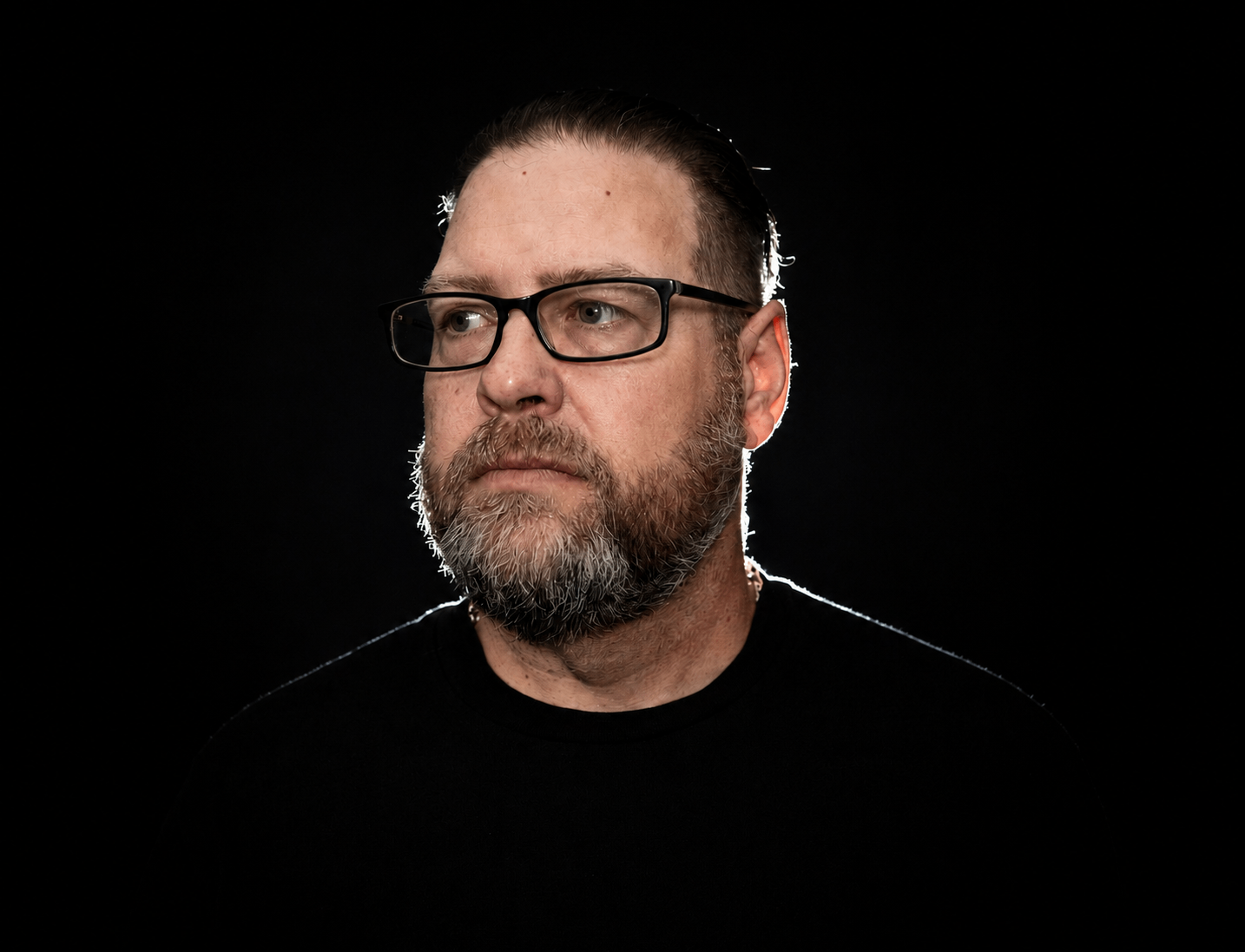 a man with glasses and a beard standing in front of a black background
