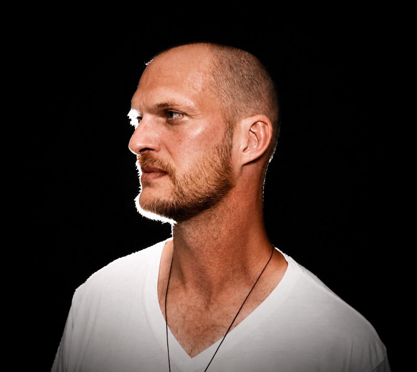 a bald man in a white v - neck shirt standing in front of a black background