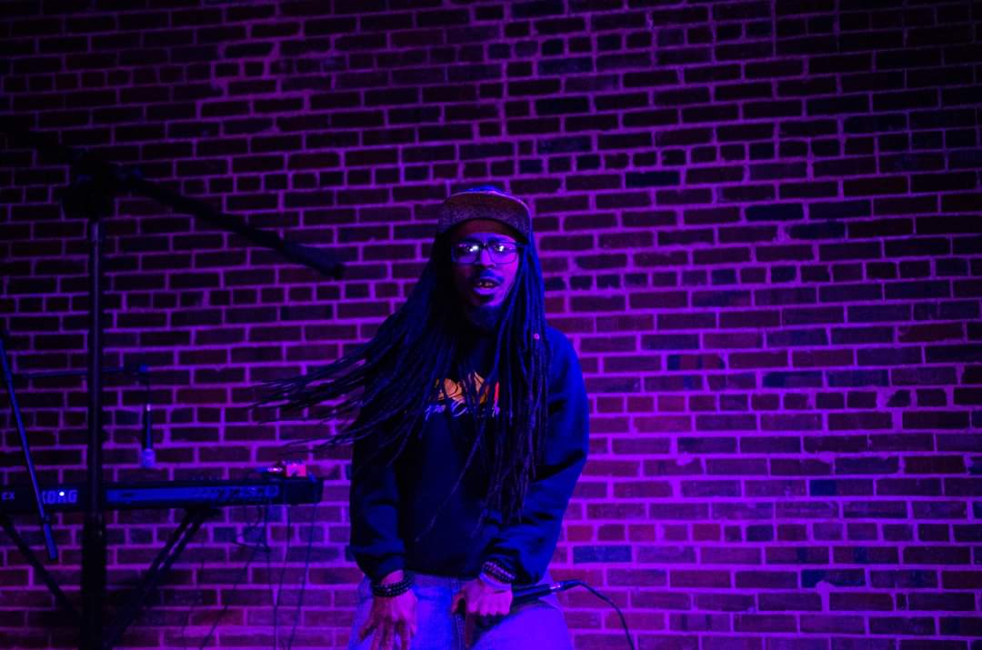 a man with dreadlocks standing in front of a brick wall