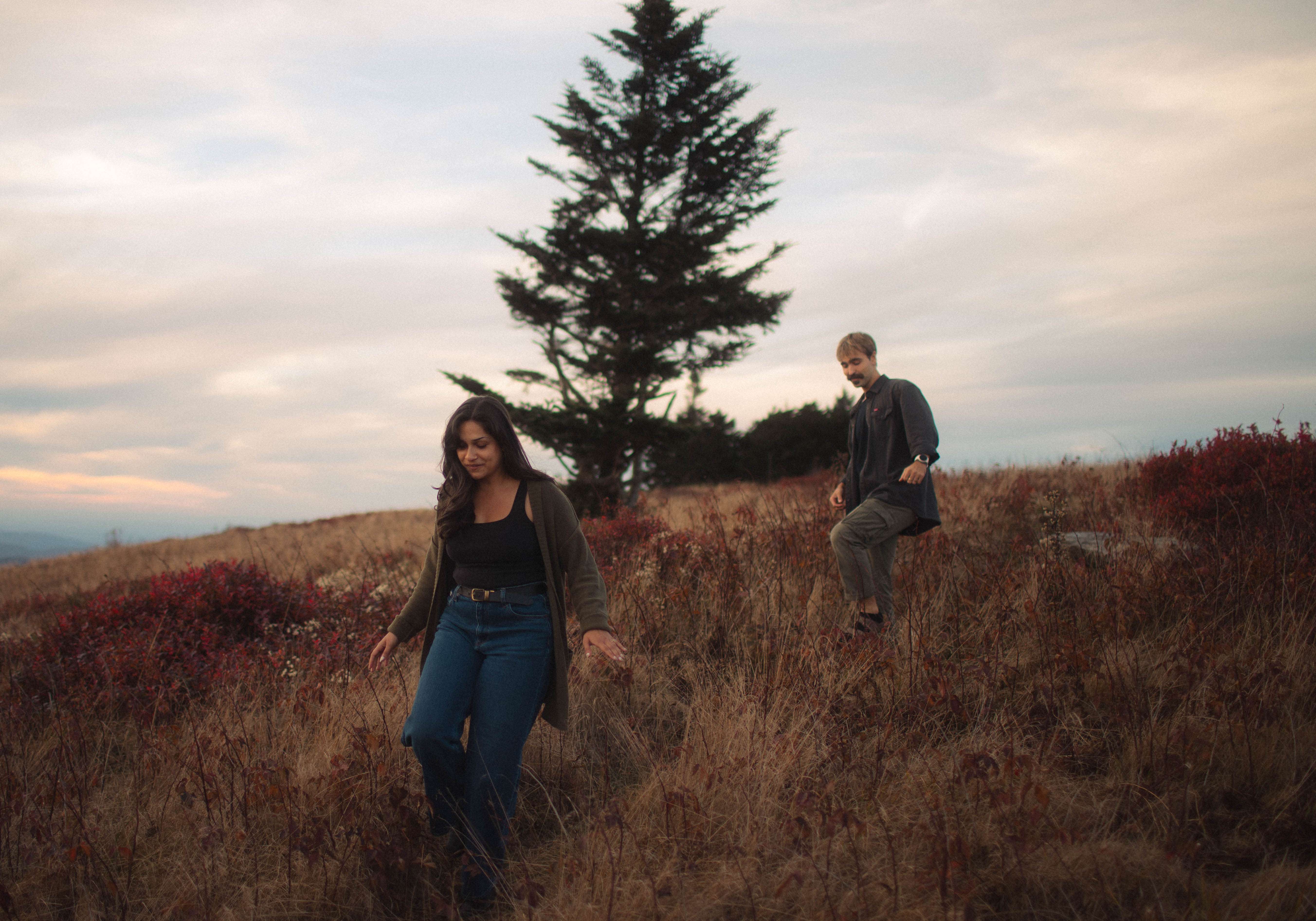 two people standing on top of a hill with a tree in the background