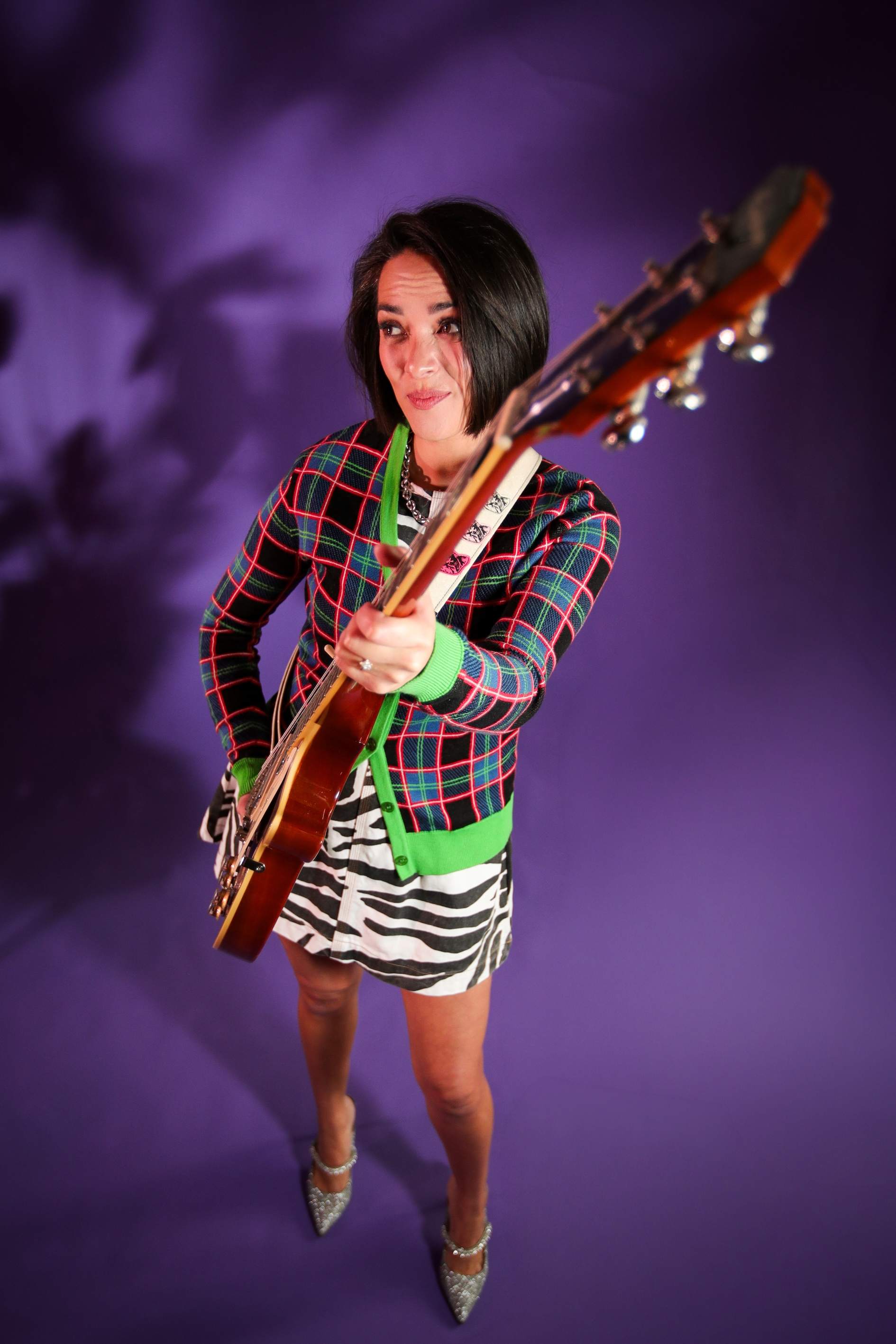 a woman holding a guitar in front of a purple background