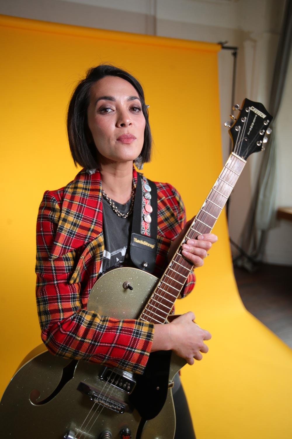 a woman holding a guitar in front of a yellow background